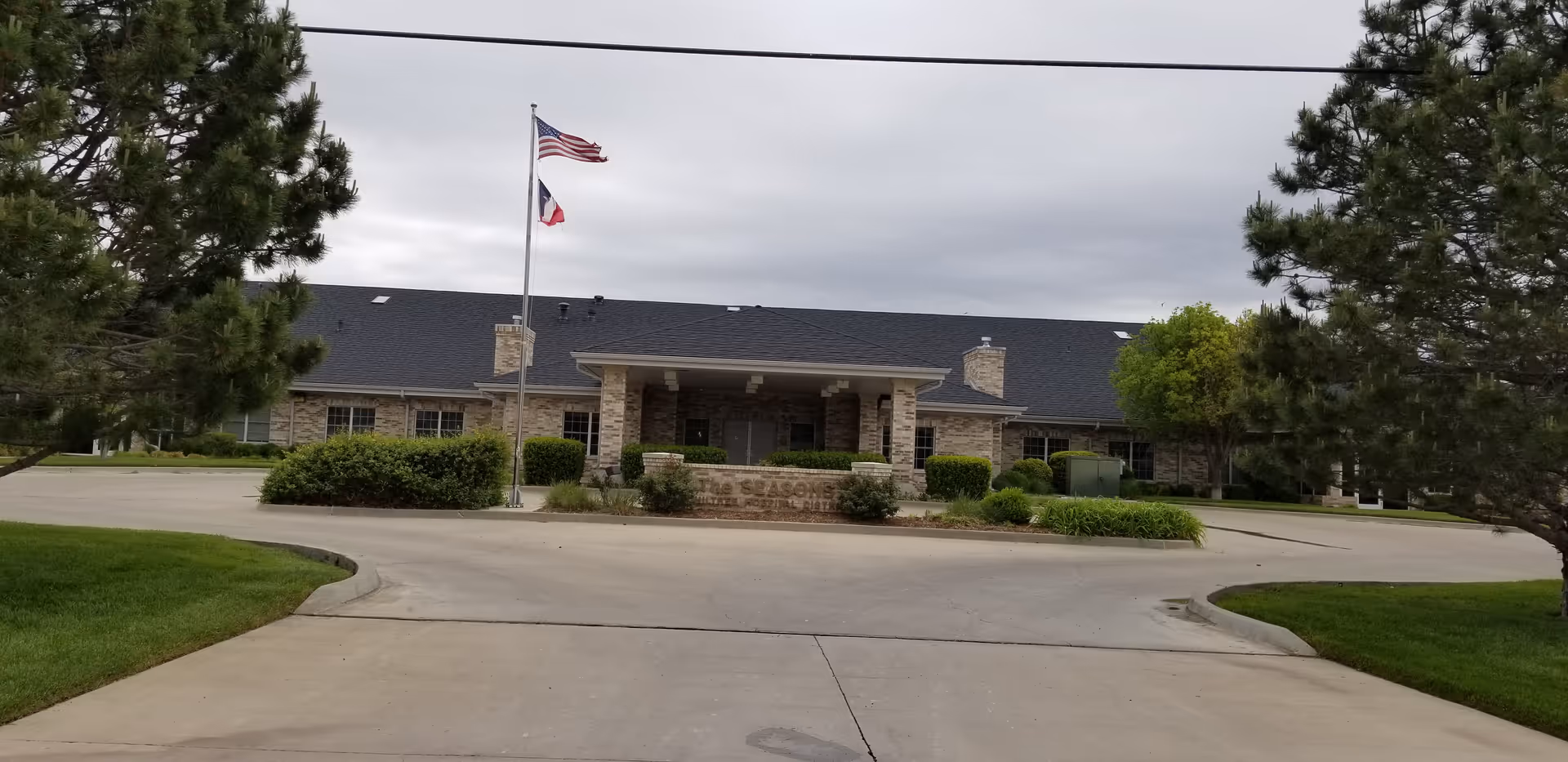 Front view of The Seasons Assisted Living building with driveway and flagpoles.