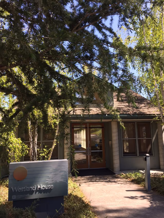 Entrance to the Westland House building with double glass doors, a sign in front, and trees partially obscuring the facade.