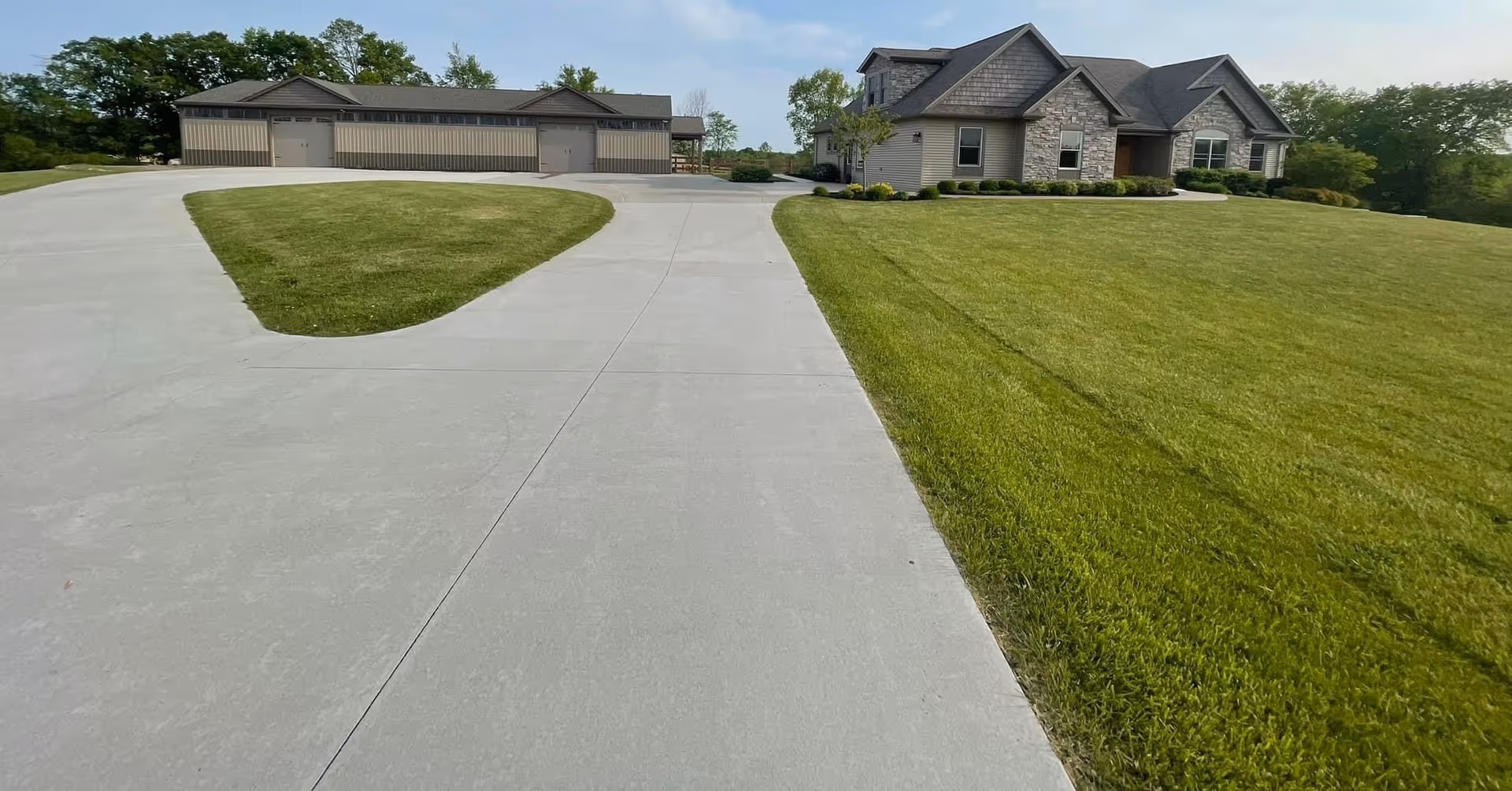 Front exterior view of a single-story house and adjacent garage with a wide concrete driveway and manicured lawn.