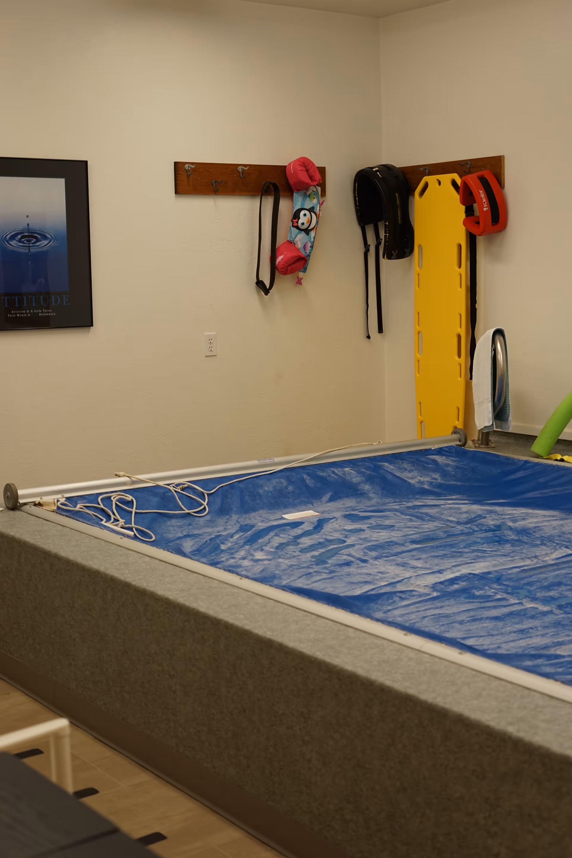 Indoor physical therapy pool area with equipment and wall hooks in a clinic room.