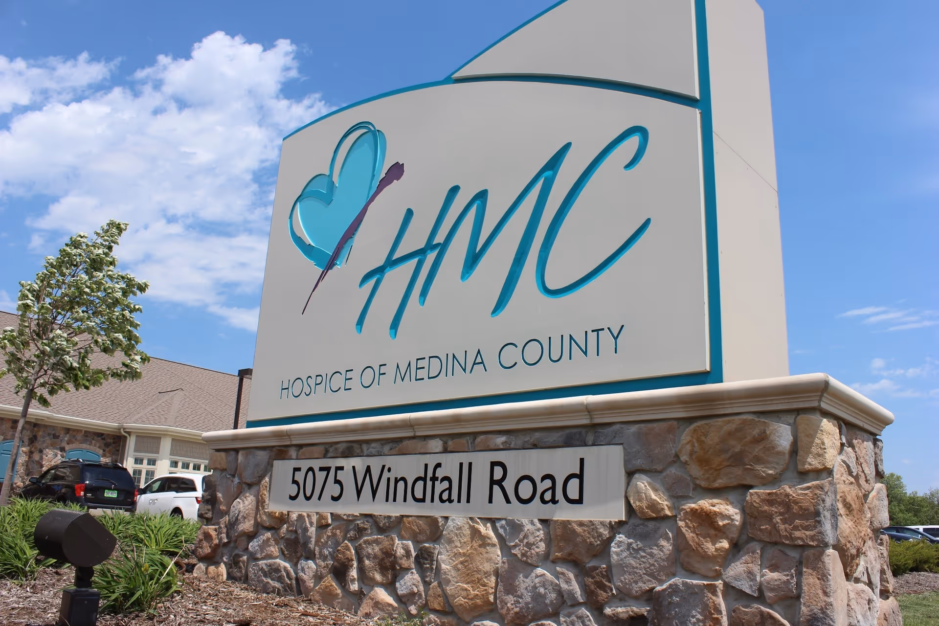 A large HMC Hospice of Medina County sign on a stone base outside a building.