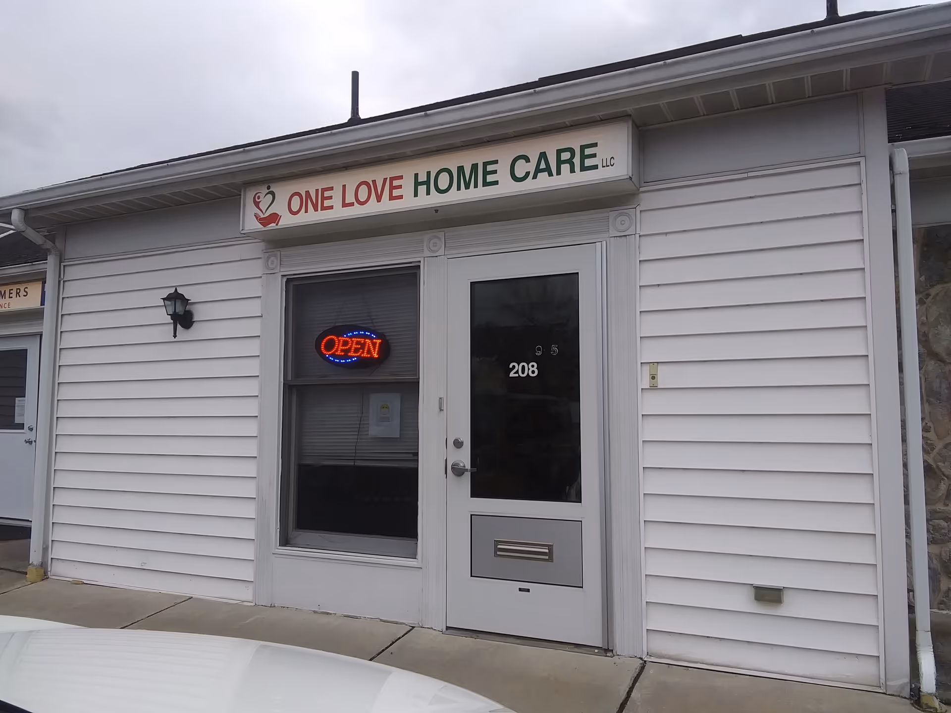 White storefront with One Love Home Care LLC sign and an open door.
