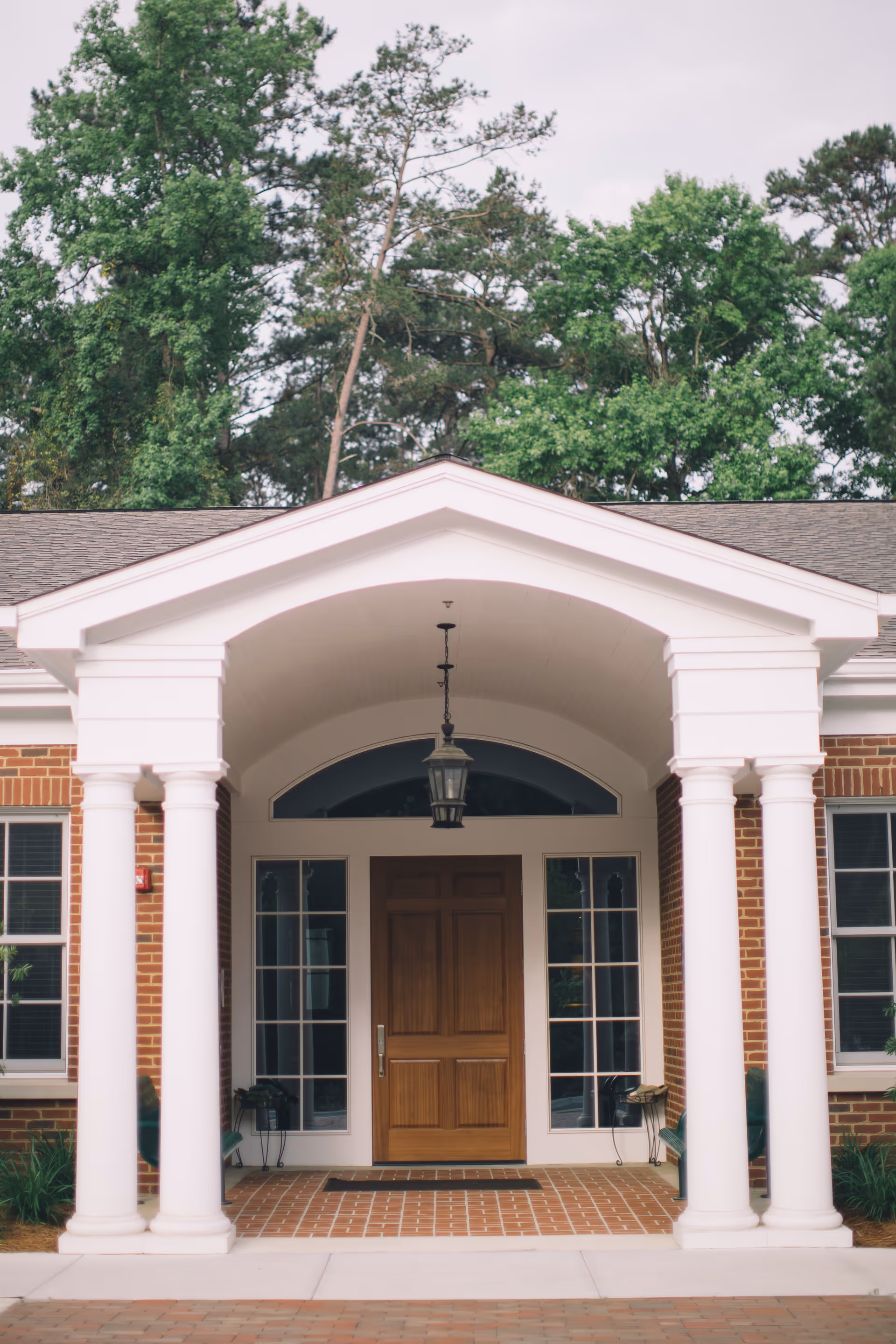 Brick facility entrance with white columns, wooden door, and a peaked porch.