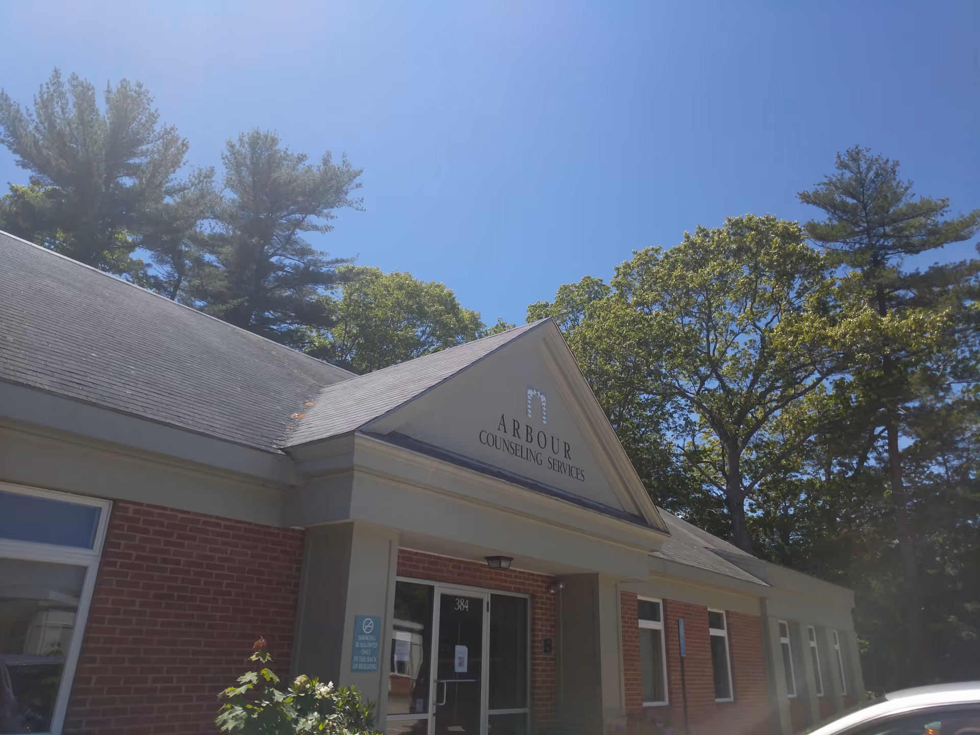 Front exterior of Arbour Counseling Services building with sign, brick walls, and surrounding trees.