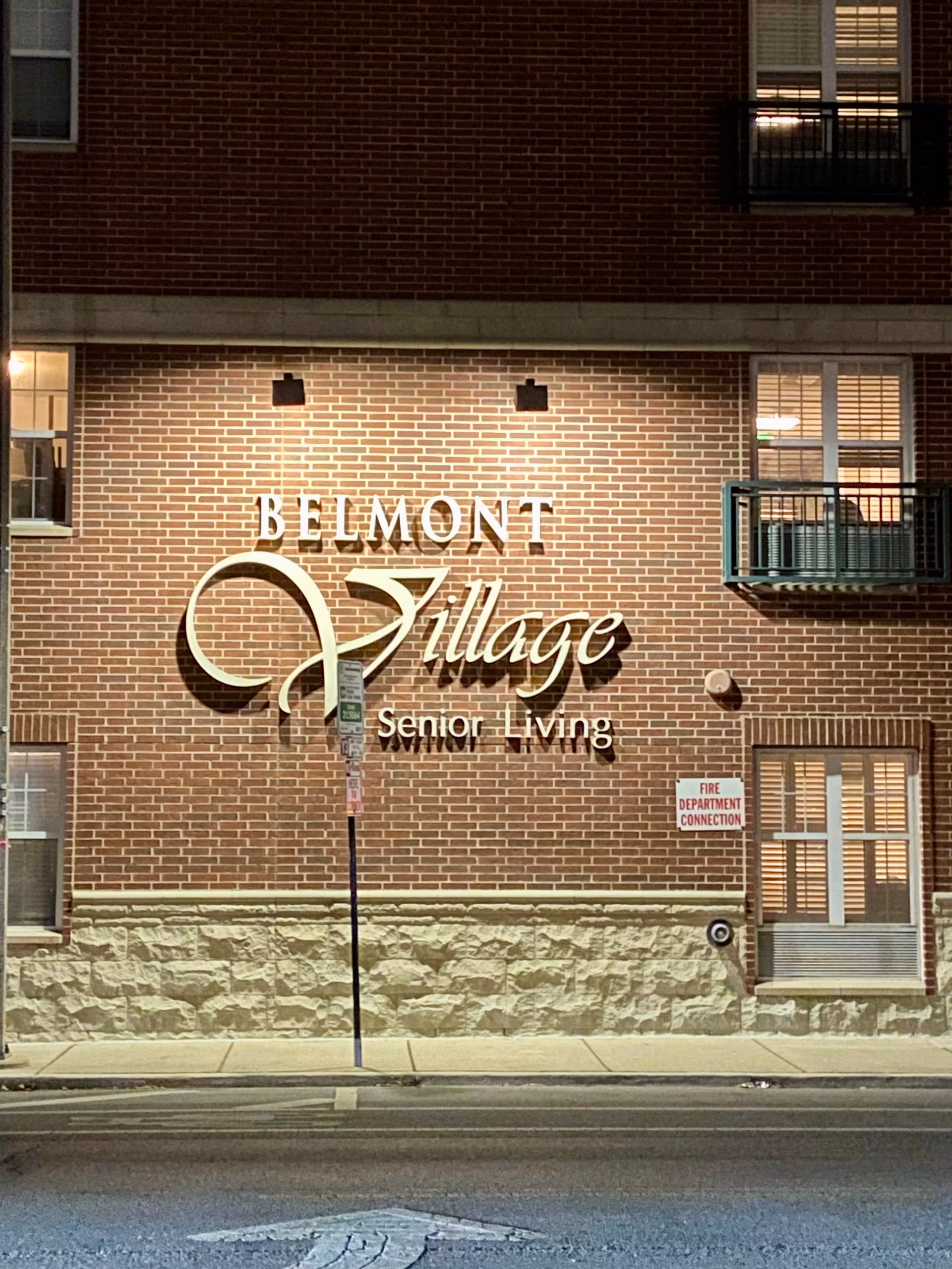 Brick building facade with Belmont Village Senior Living sign along a city street.