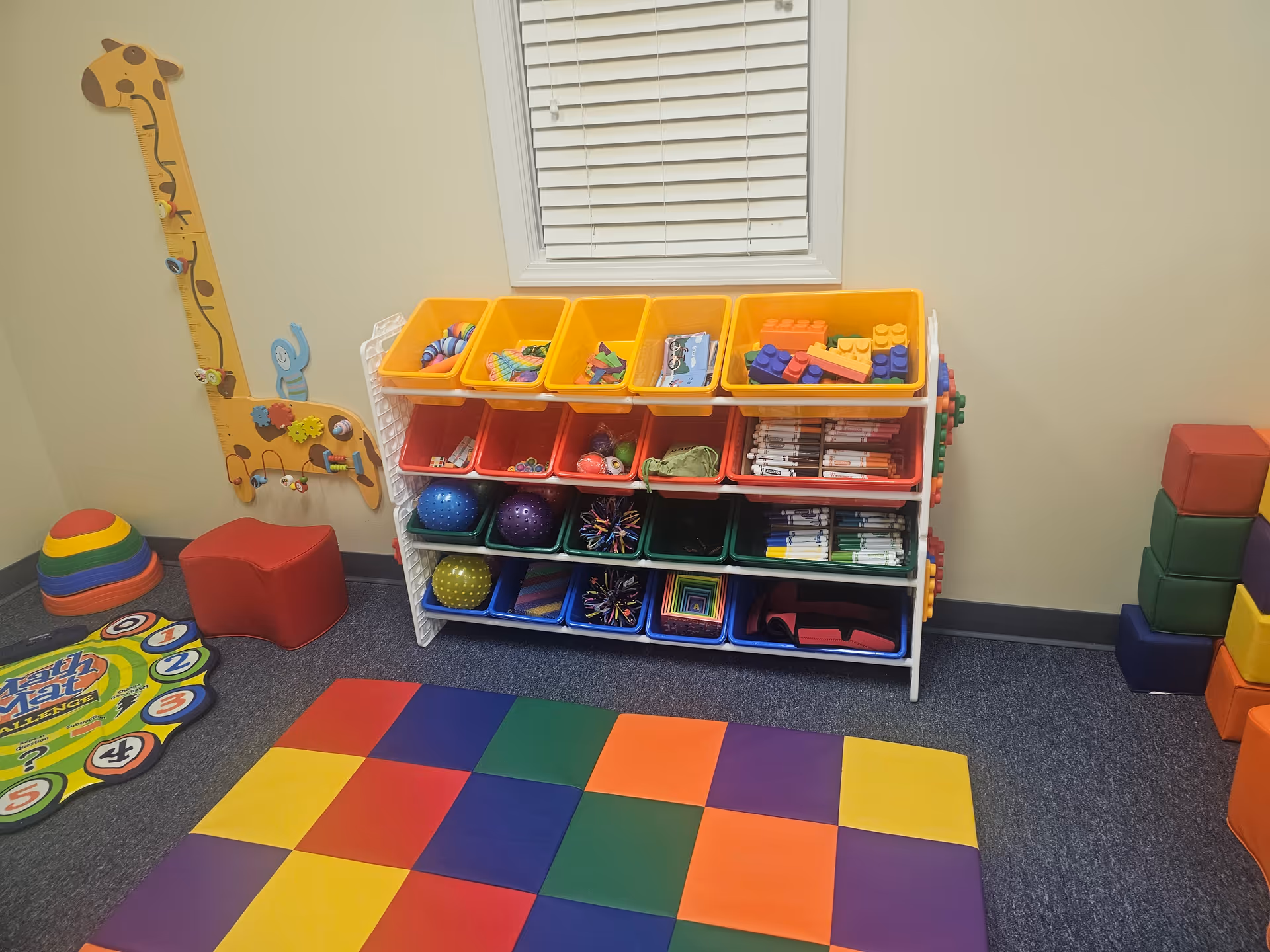 Colorful children's play area with stacked bins, mats, blocks, and wall decor.