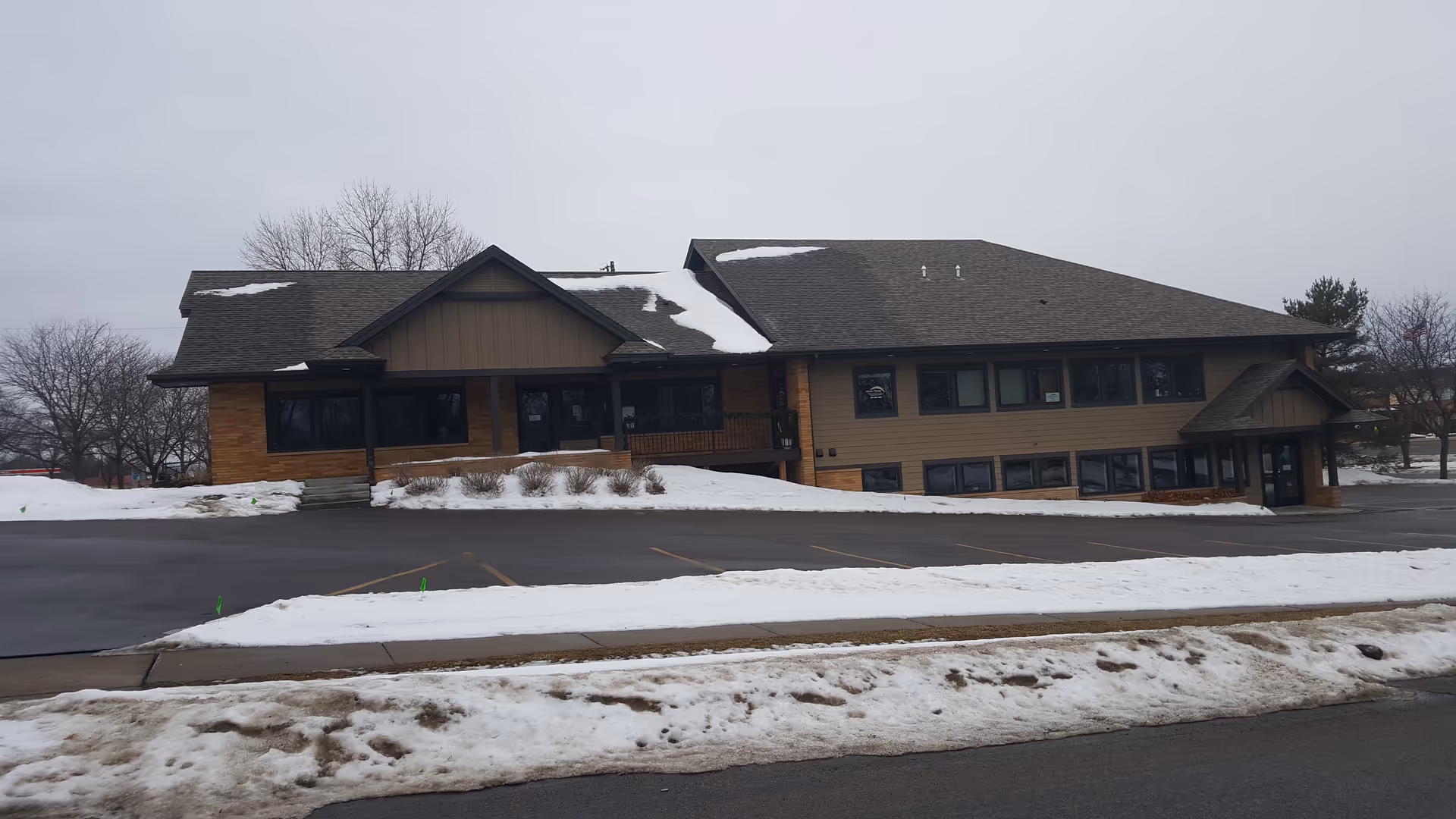 Exterior view of a brown, two-story senior living facility with snow on the parking lot.