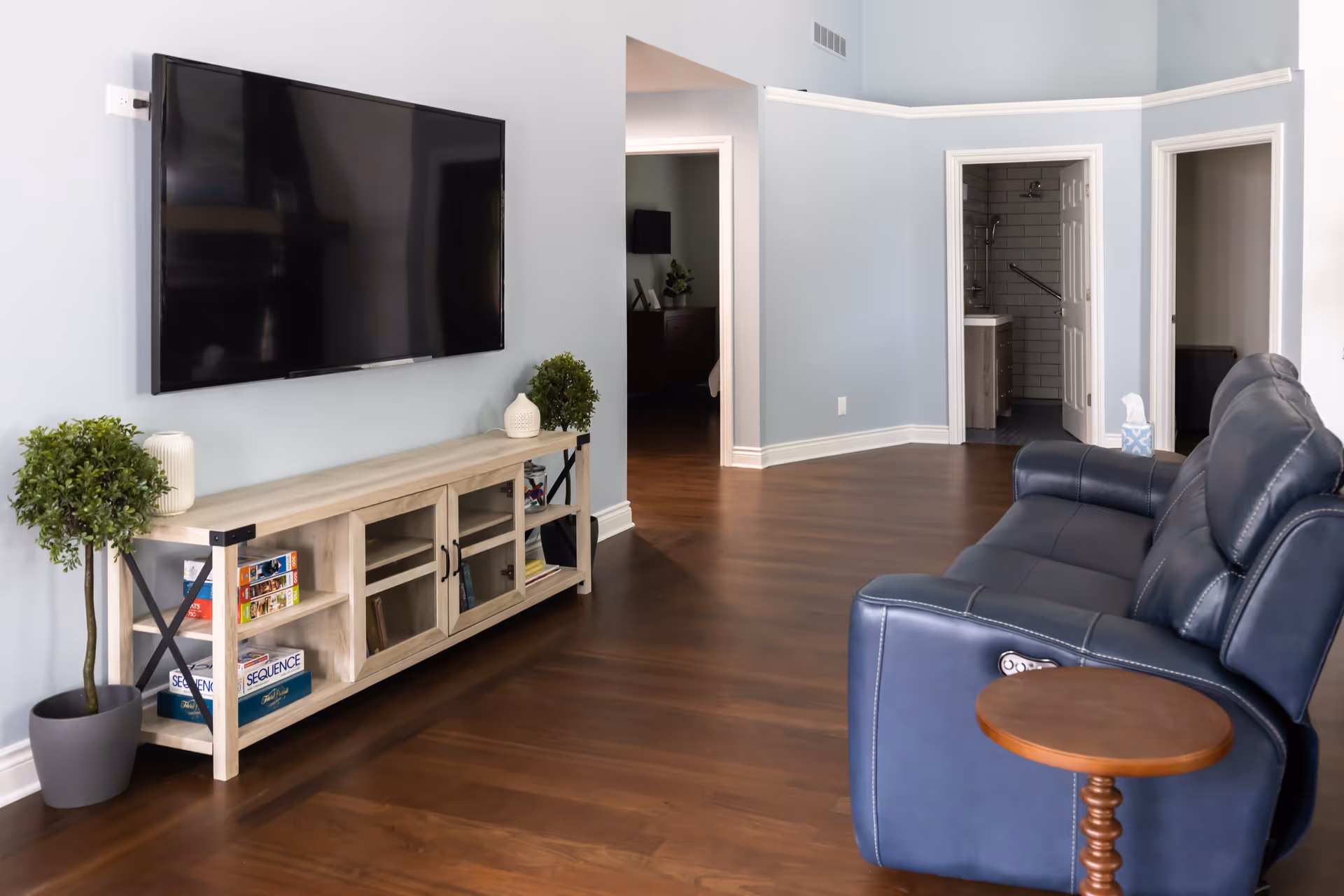 Modern living room with wall-mounted TV, blue walls, hardwood floor, and blue leather sofa.