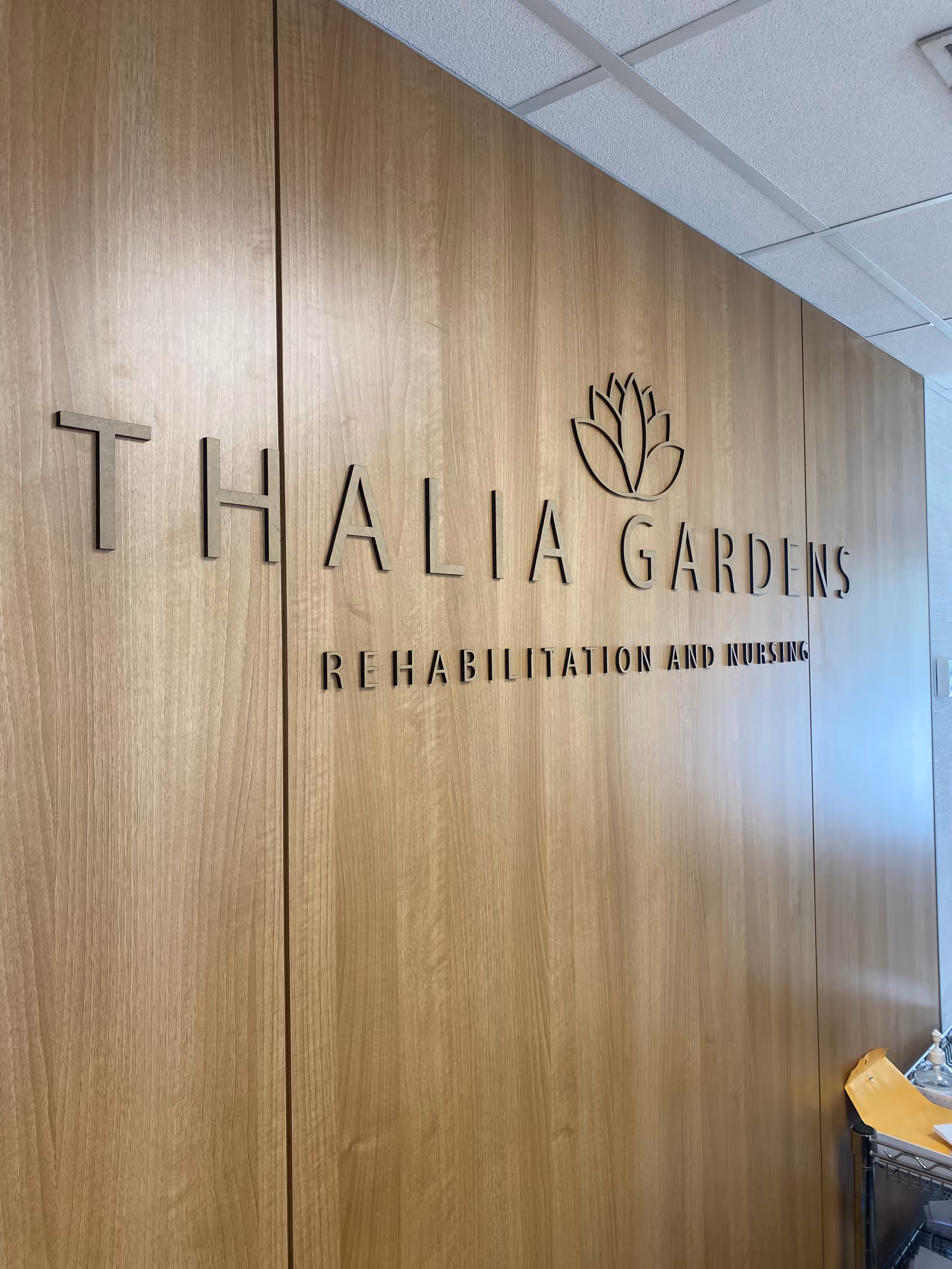 Wood-paneled wall with Thalia Gardens Rehabilitation and Nursing signage and a floral logo.