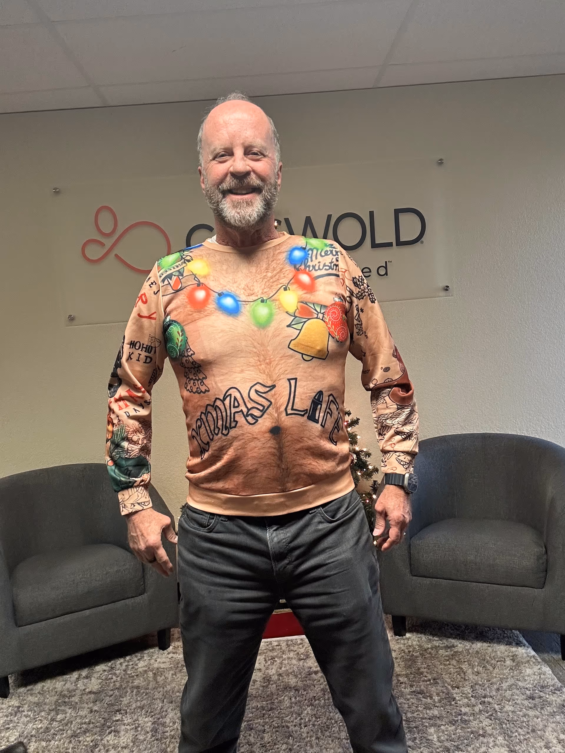 Smiling man in a holiday sweater stands in a lounge area.