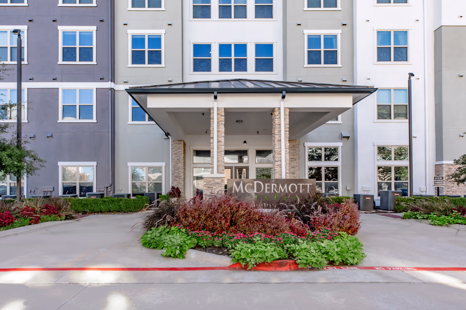 Entrance portico of a multi-story senior living building with a sign reading "McDermott" and landscaped plants in front.