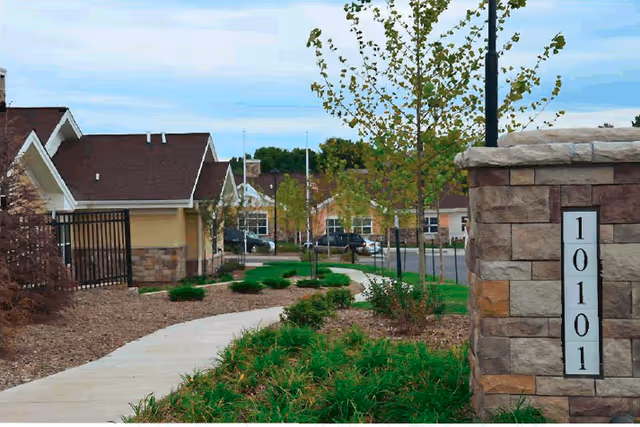 Exterior view of The Heritage of Overland Park with a stone pillar, walkway, and landscaping.
