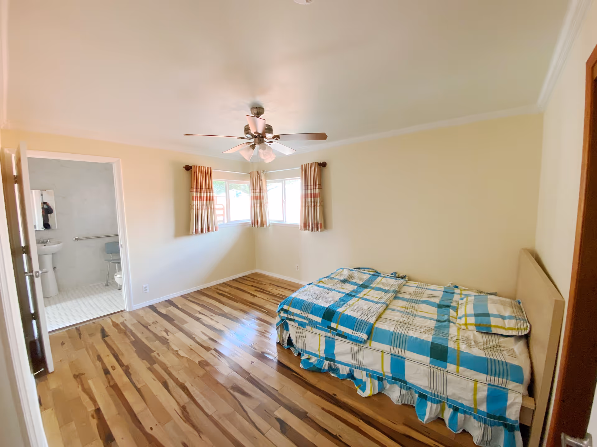Bedroom in a senior living facility with bed, windows, curtains, and an adjacent bathroom.