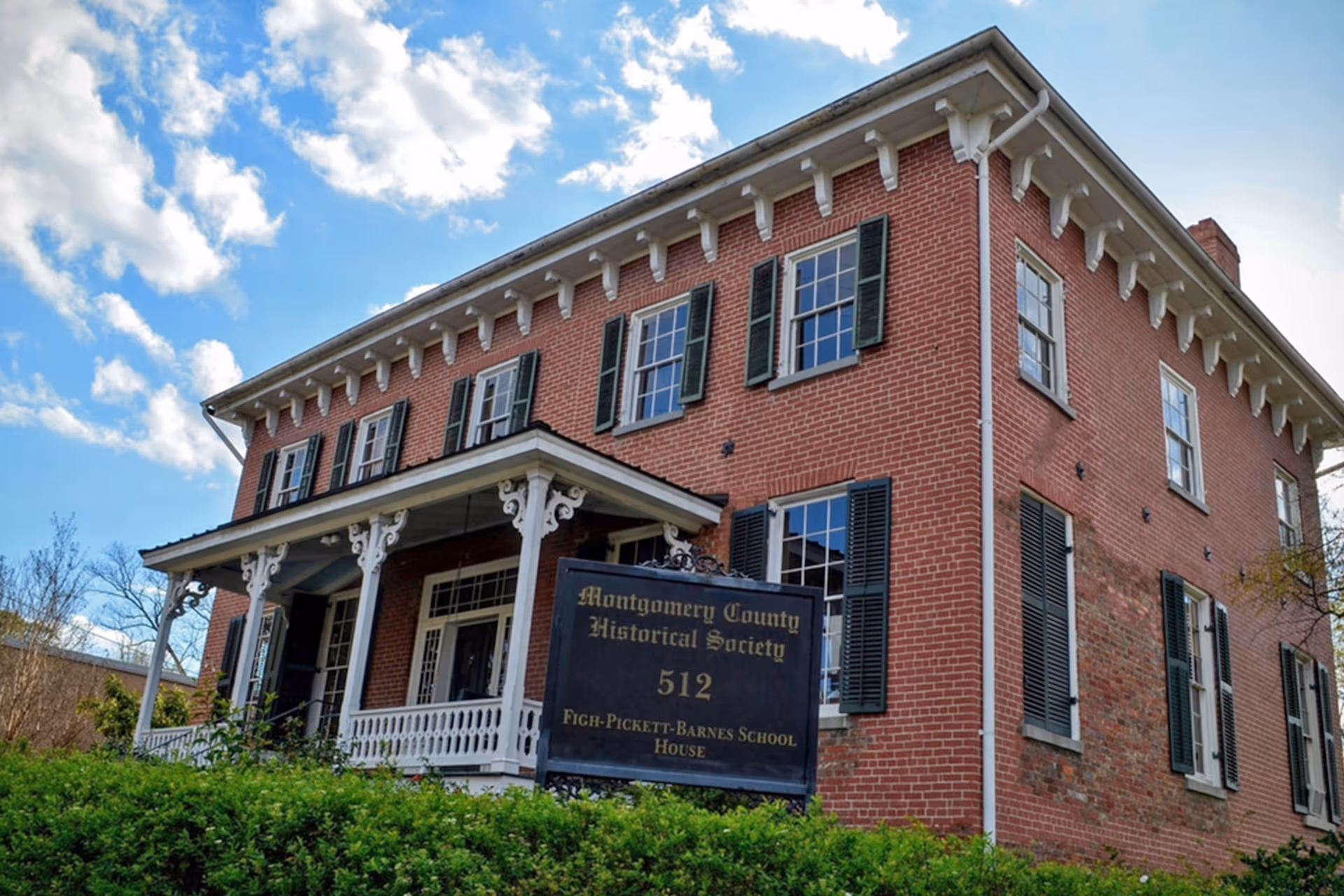 Red brick two-story building with a porch and a historical society sign