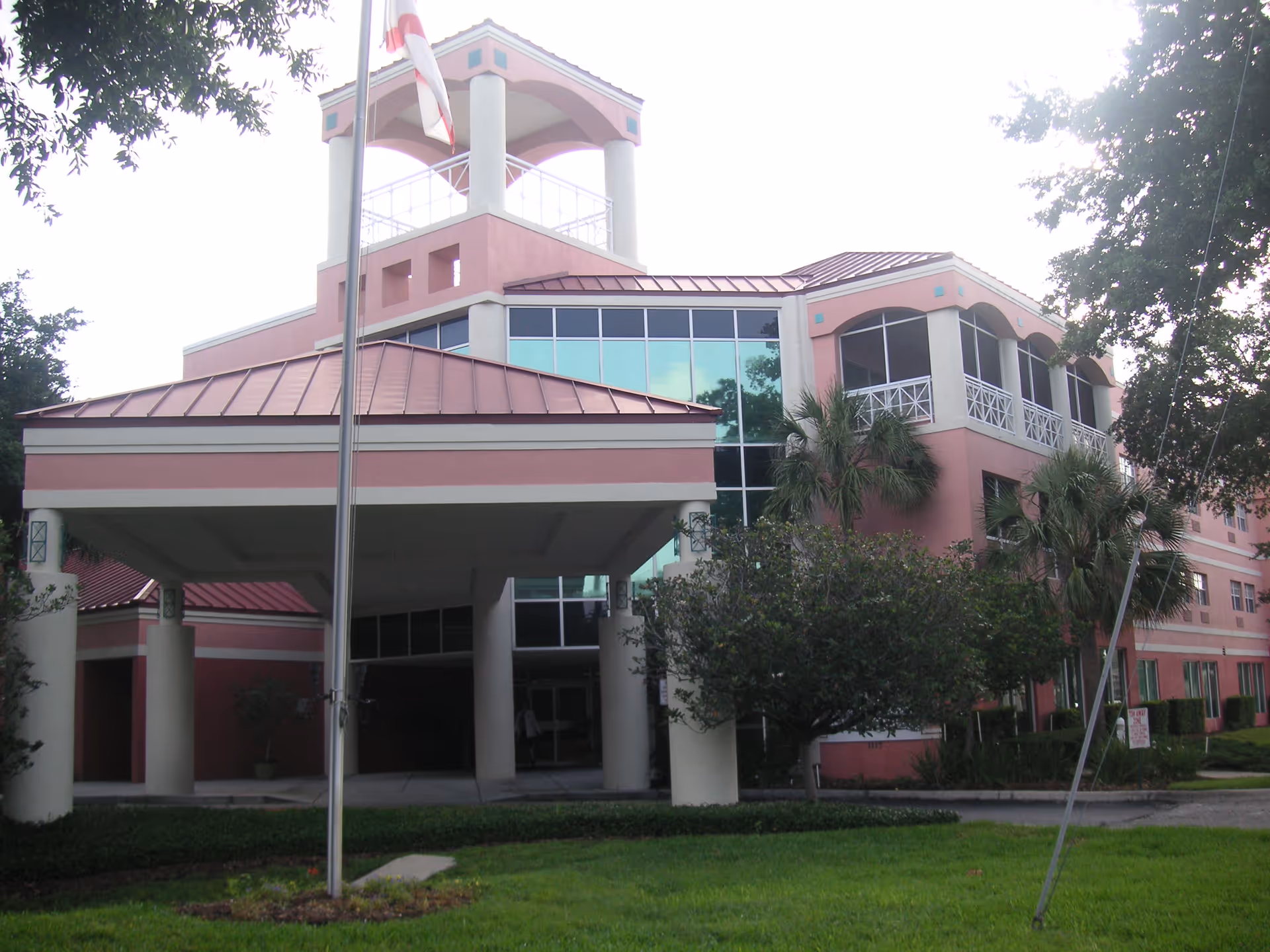 Pink multi-story nursing home exterior with glass entrance and landscaping.