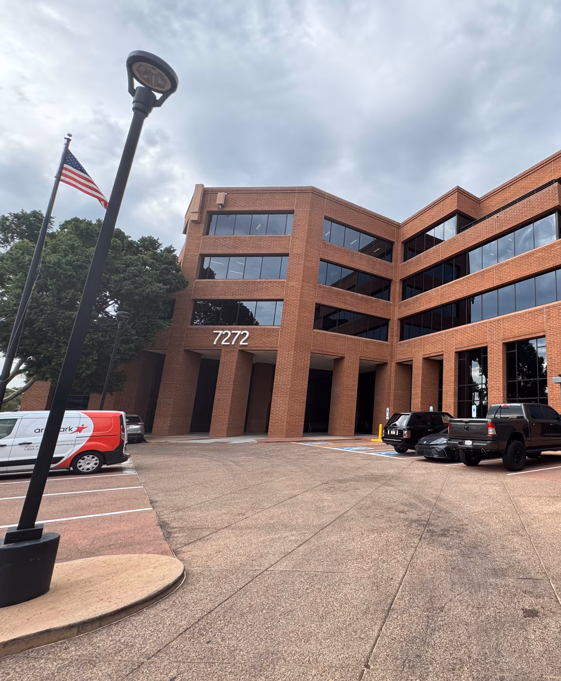 Red brick, multi-story building with large glass windows and a parking lot in front.