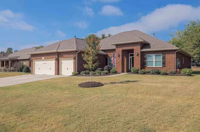 Single-story brick senior living facility with manicured lawn and a flag by the entrance.