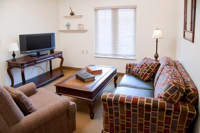 Cozy living room with patterned sofa, coffee table, TV stand, and window blinds.