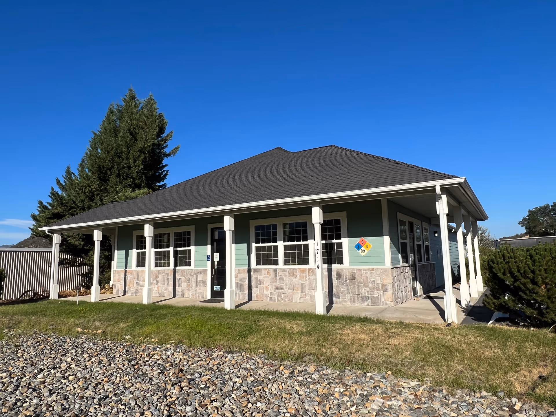 A single-story building with green siding, stone base, white columns, and a blue sky.