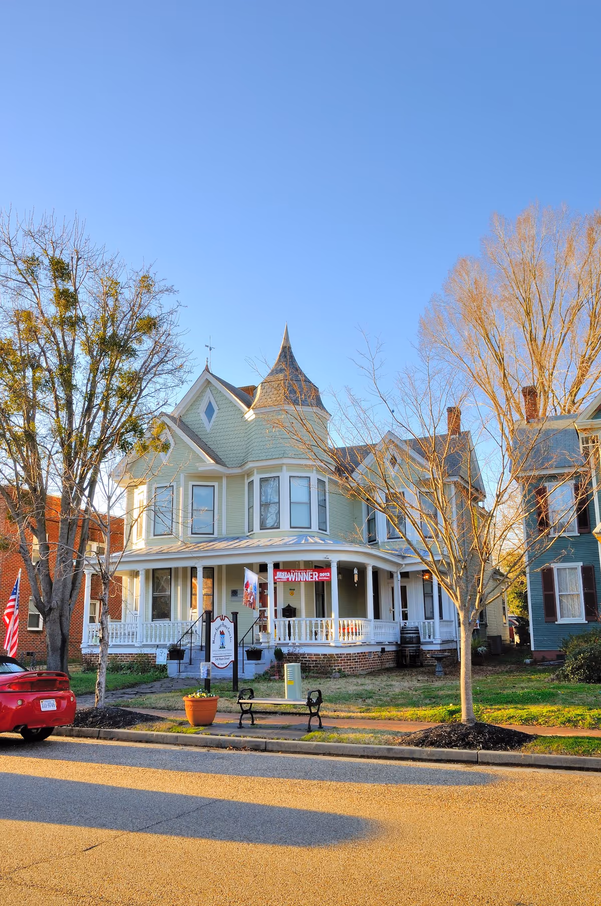 Two-story Victorian-style house with wraparound porch on a sunny street.