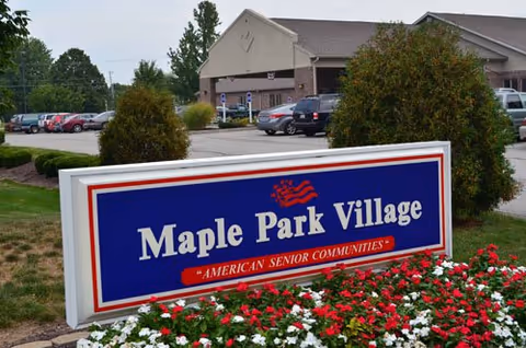 Maple Park Village sign with flower beds, shrubs, and a parking lot in front of building