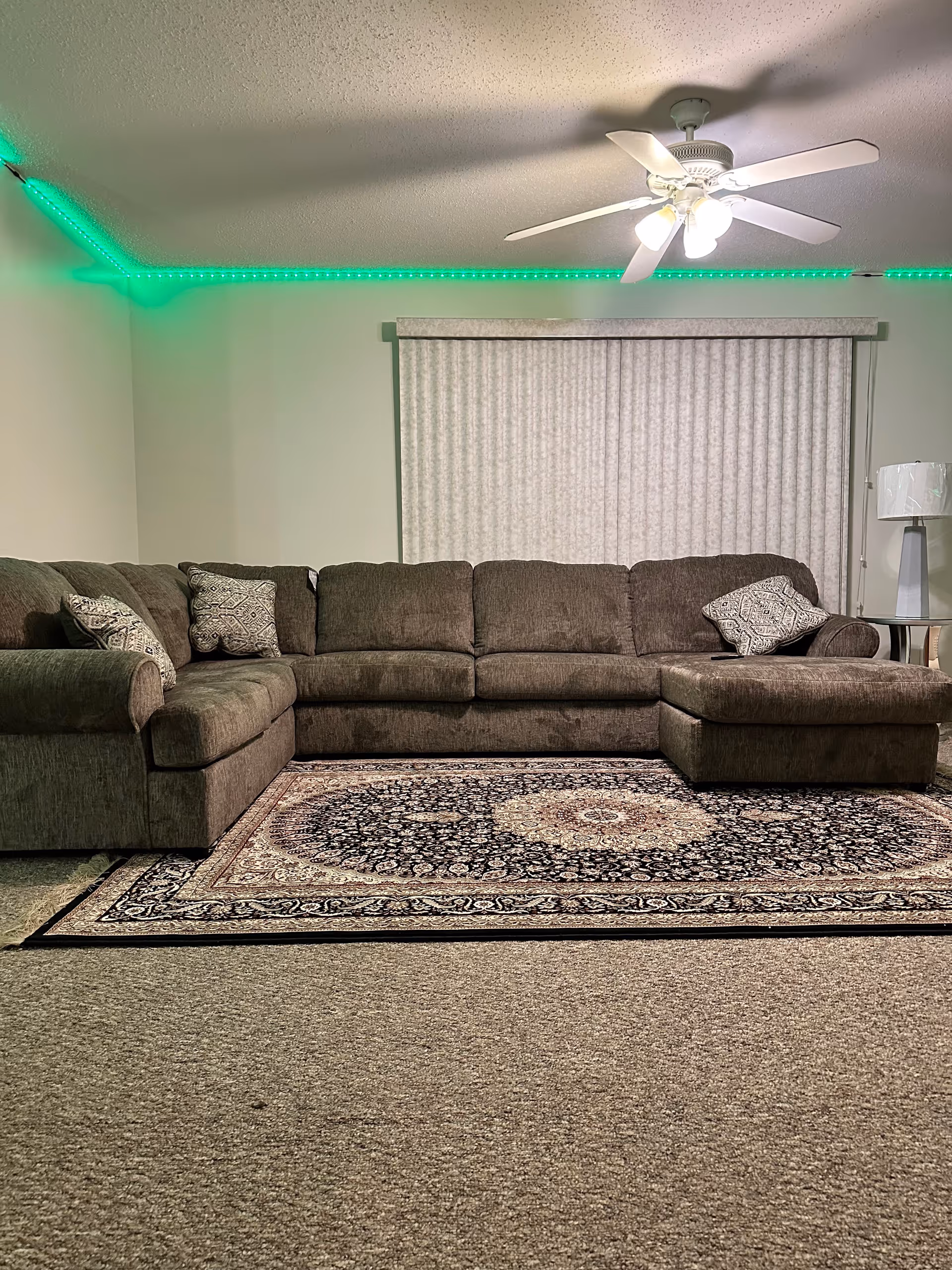 Large gray sectional sofa in a living room with a ceiling fan and rug.