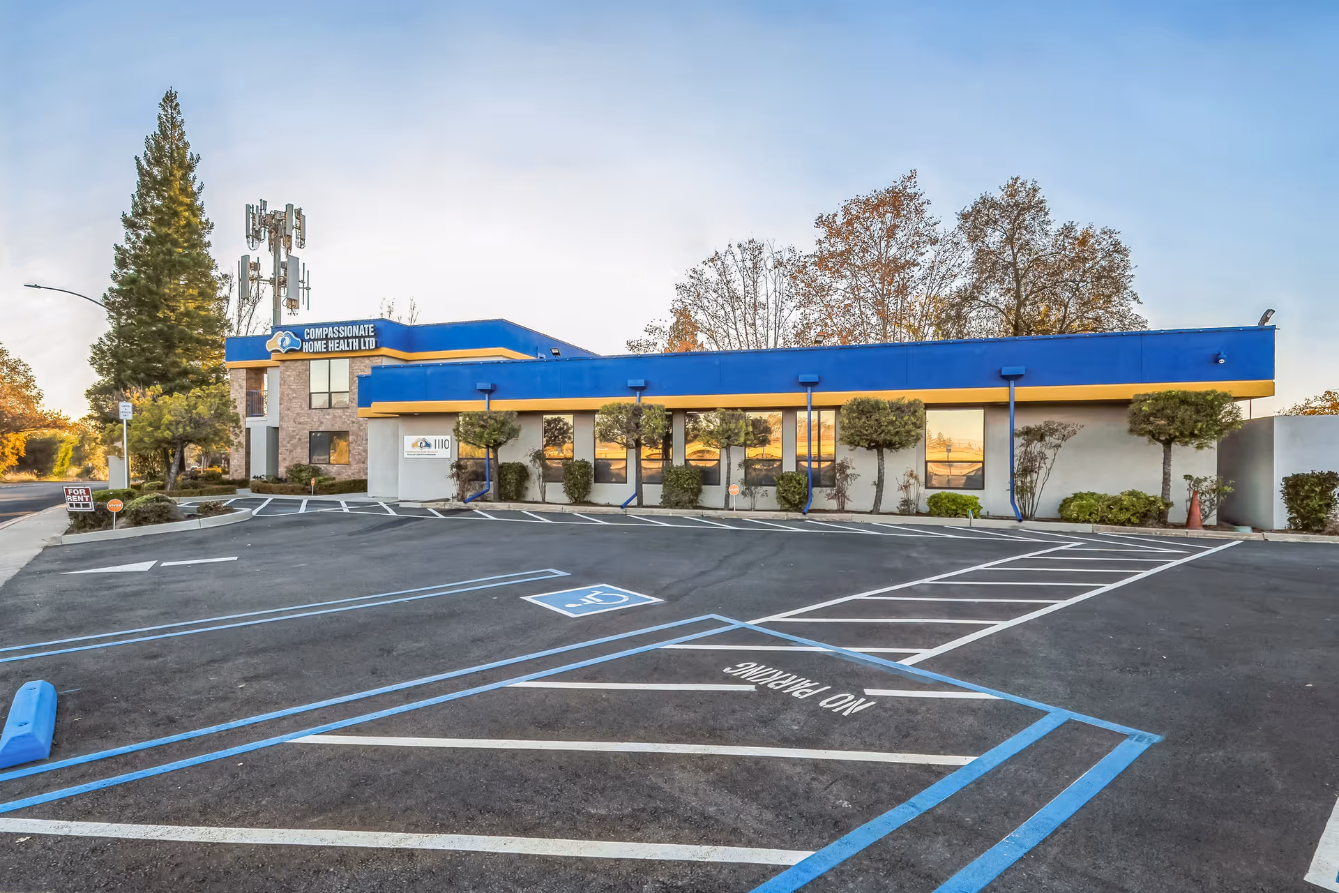 Front exterior of Compassionate Home Health Ltd building with blue and yellow trim and parking.