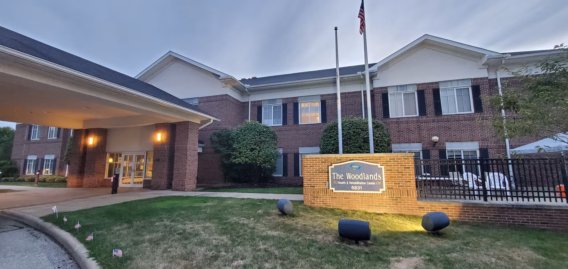 Brick exterior of Woodlands Health and Rehab Center with entrance, flagpoles, and sign.