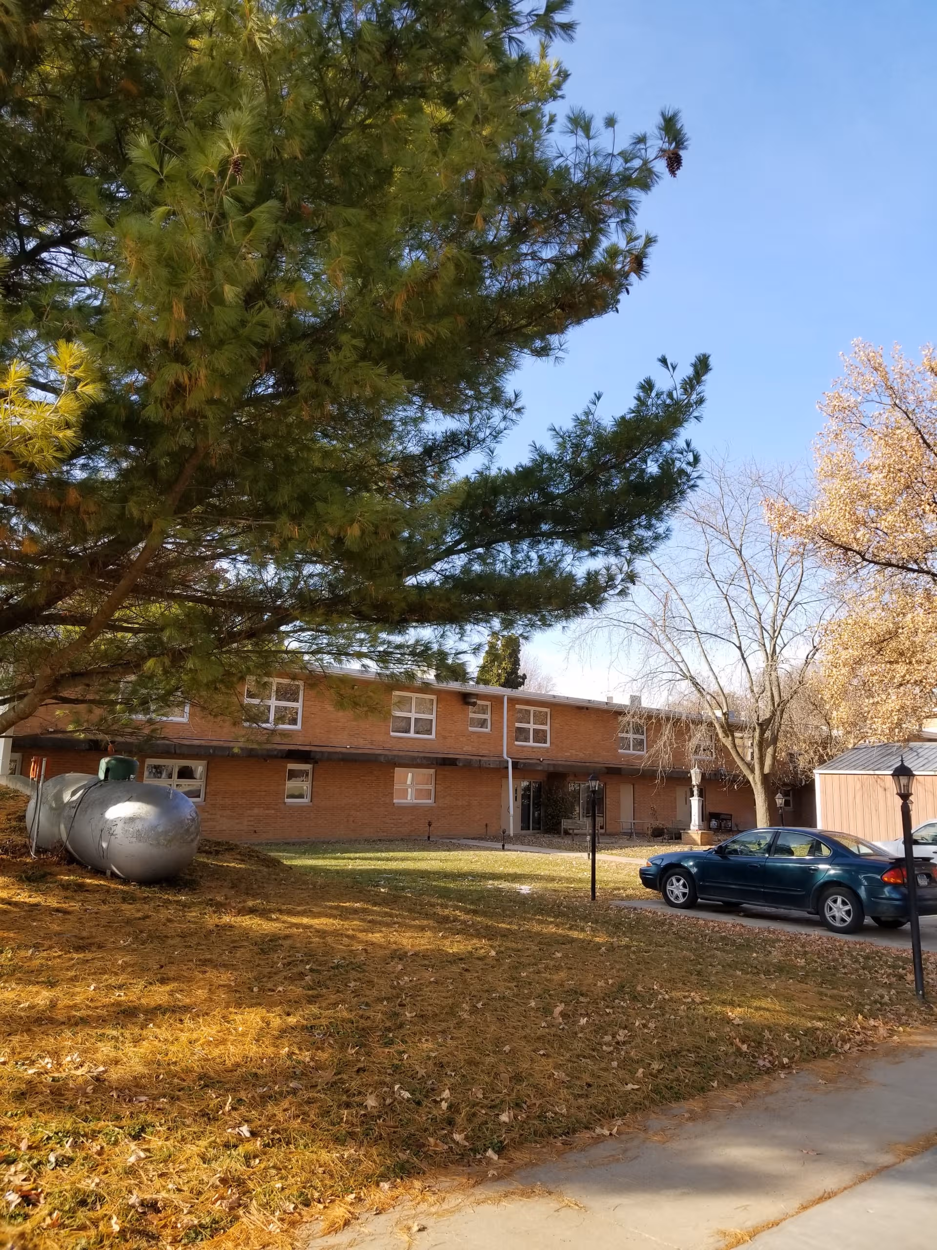 Exterior view of Rushville Nursing and Rehab Center with trees, car, and propane tank.