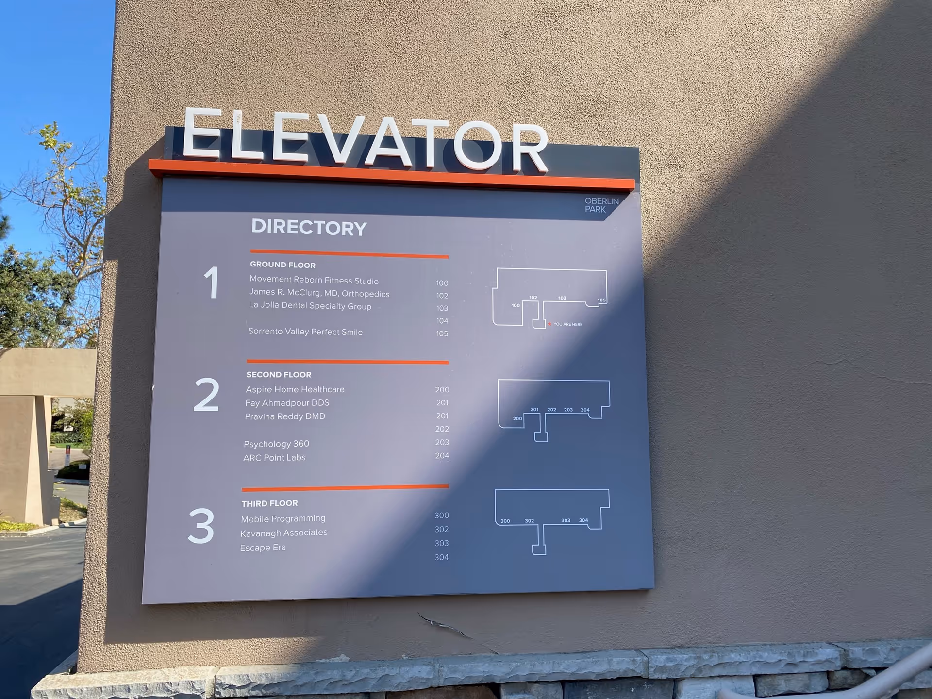 Outdoor wall with a large elevator sign and directory listing floors.