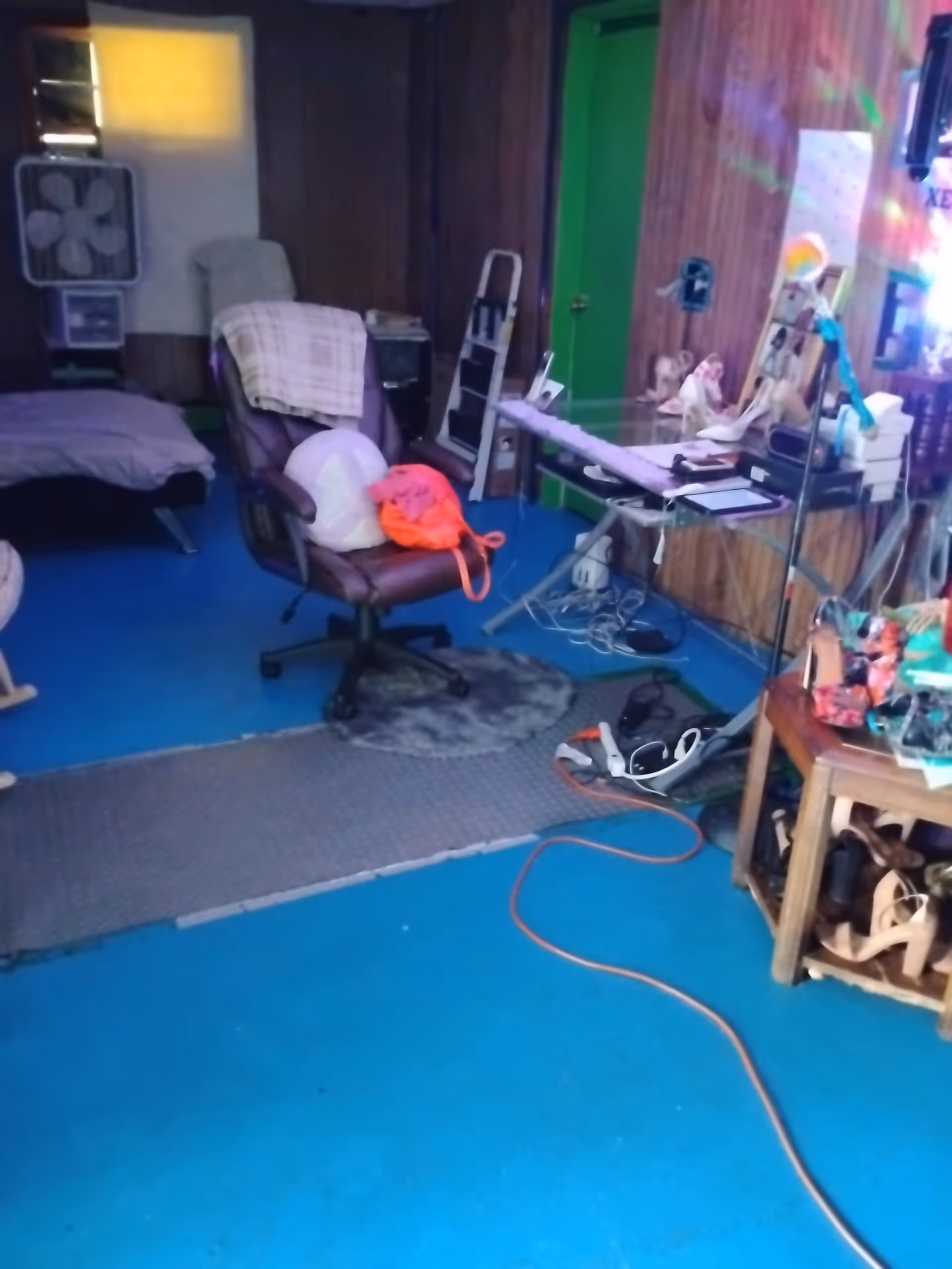 A cluttered blue-floored senior room with bed, desk, chair, and scattered items.