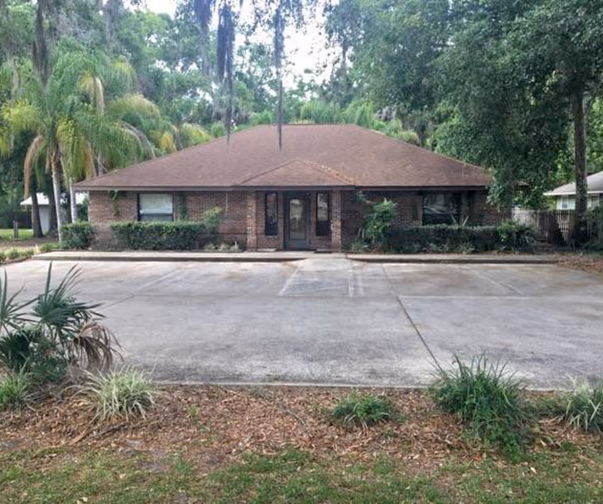 Brick, single-story building with a brown roof, surrounded by trees and a parking lot.