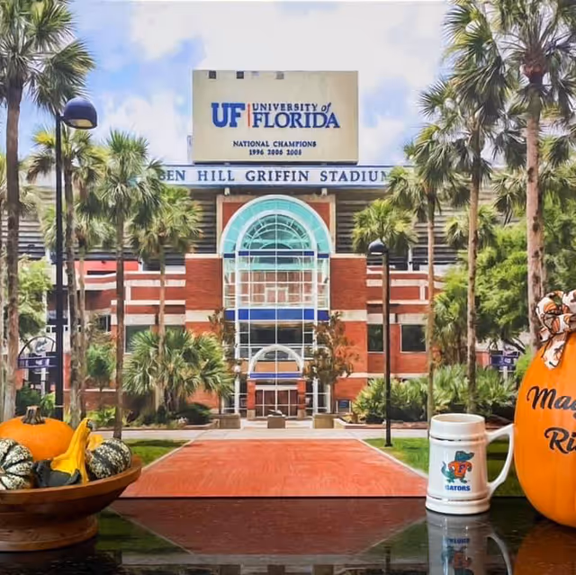Front view of a university building with palm trees, autumn pumpkins, and a gator mug.