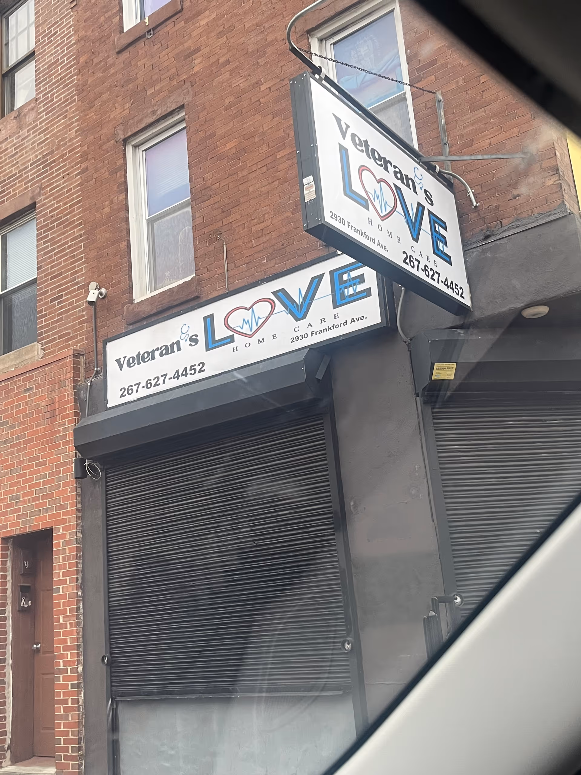 Brick storefront with Veteran's Love Home Care signs and closed metal shutters.