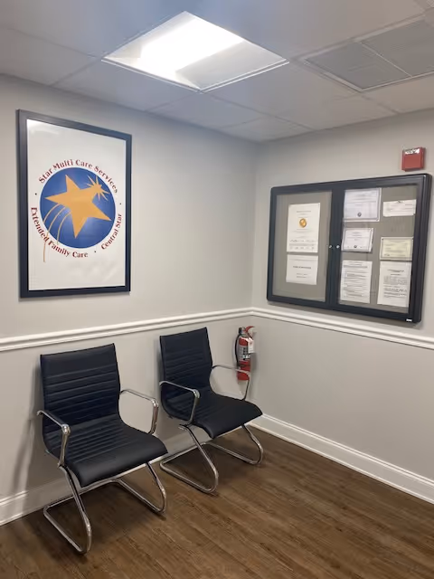 A small gray-walled waiting area with two black chairs and a bulletin board.