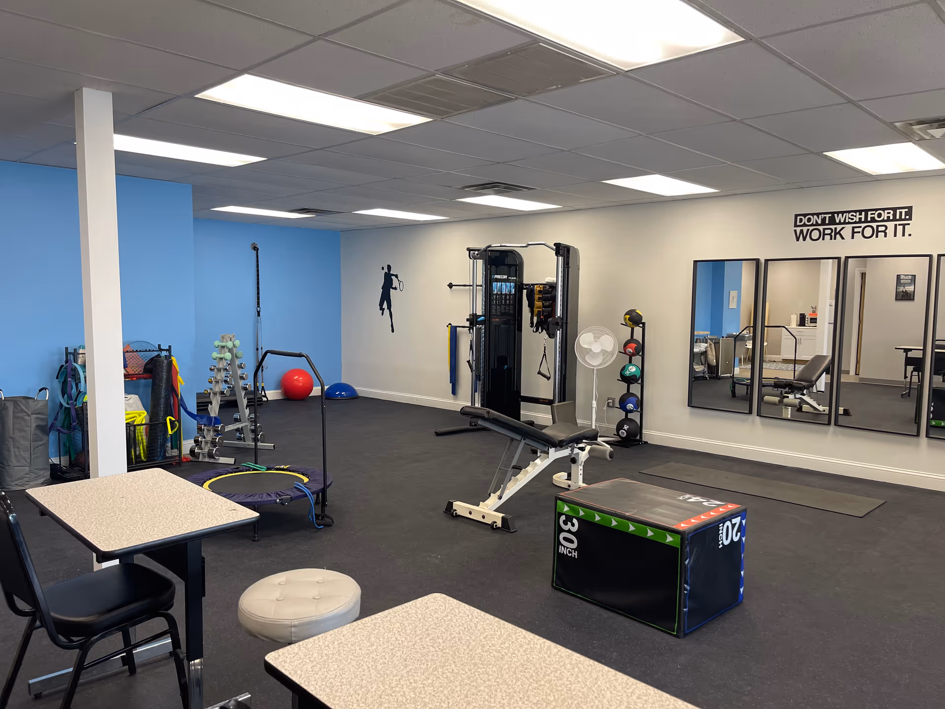 Bright rehab gym with benches, weights, mats, exercise equipment, and wall mirrors.