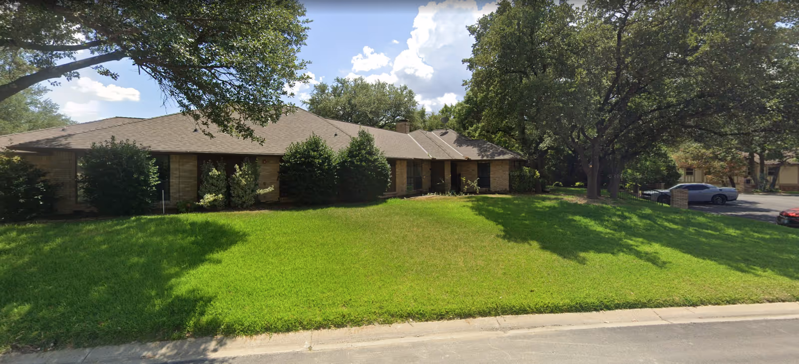 Exterior of a single-story senior living facility with a green lawn and trees.