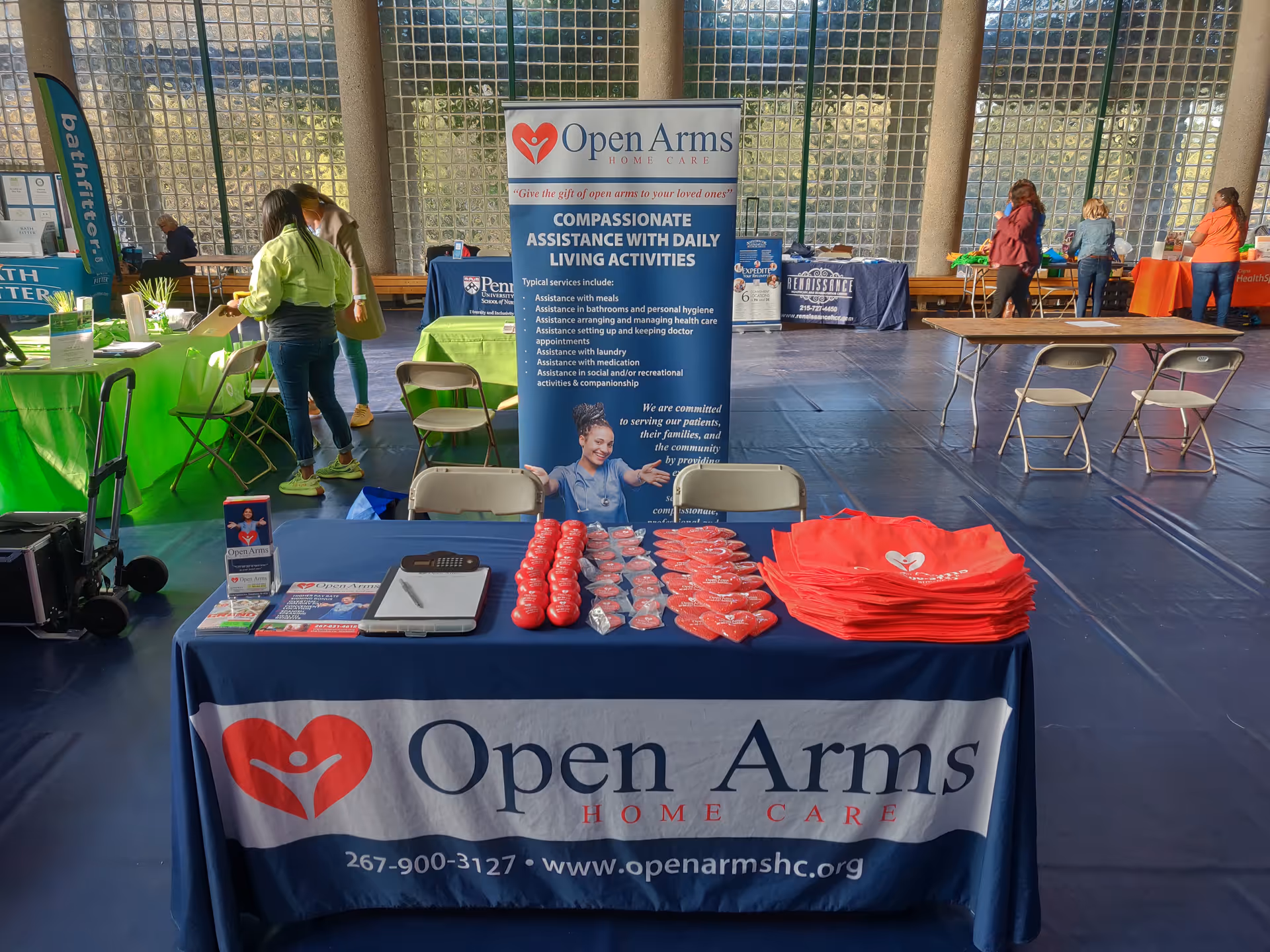 Open Arms Home Care booth indoors with tables, banners, and promotional items.