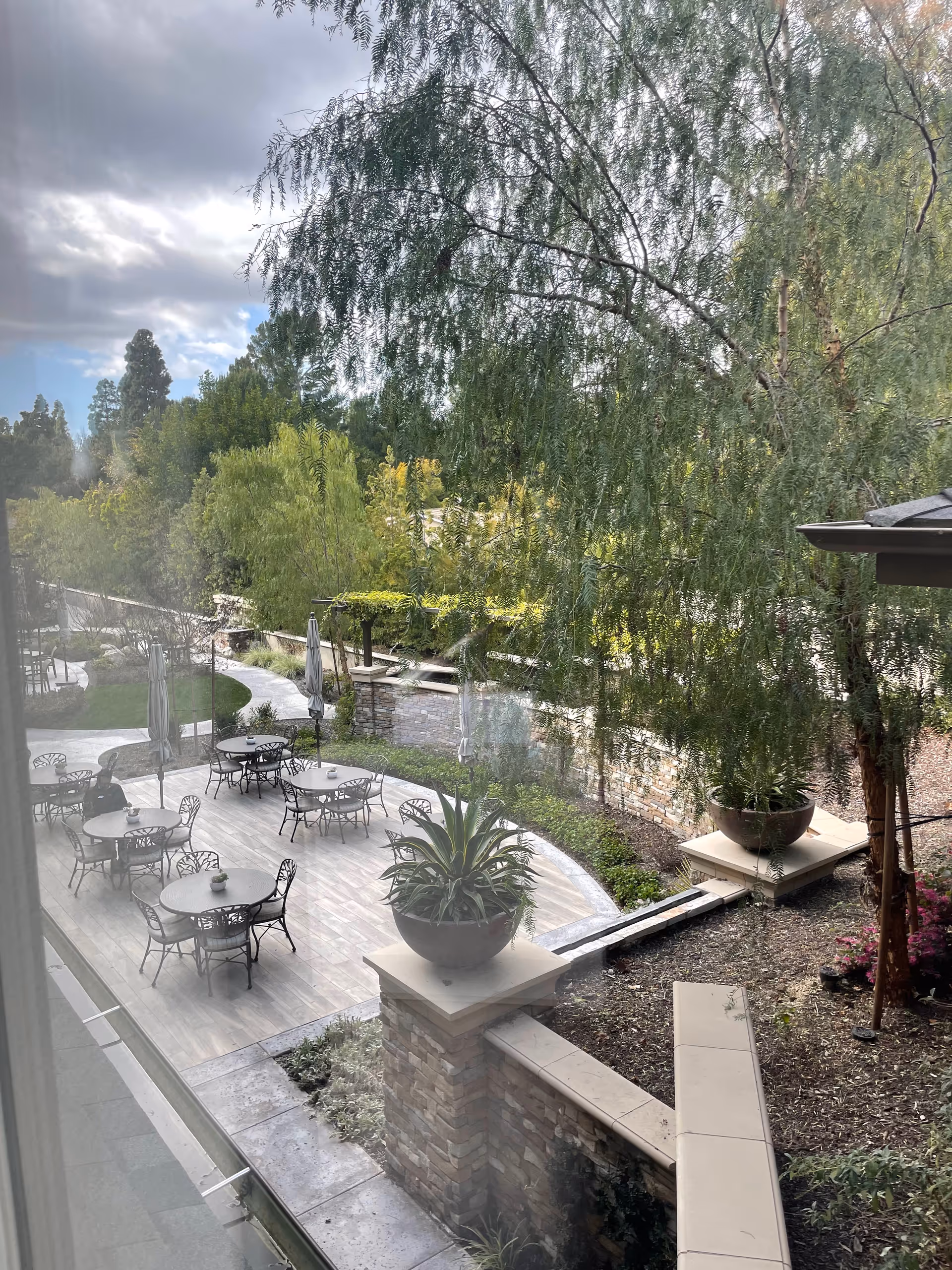 Outdoor courtyard with round metal tables, chairs, umbrellas, and lush greenery.