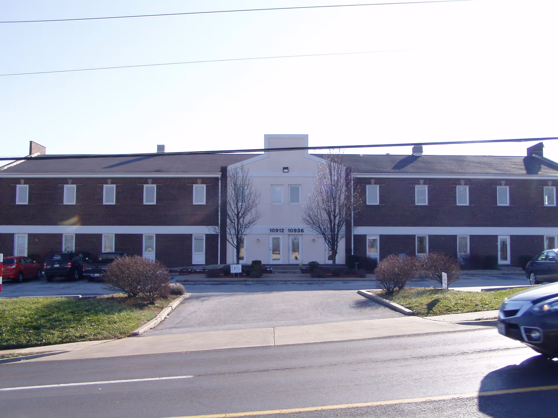 Brick senior living facility front entrance with parked cars and landscaped approach.