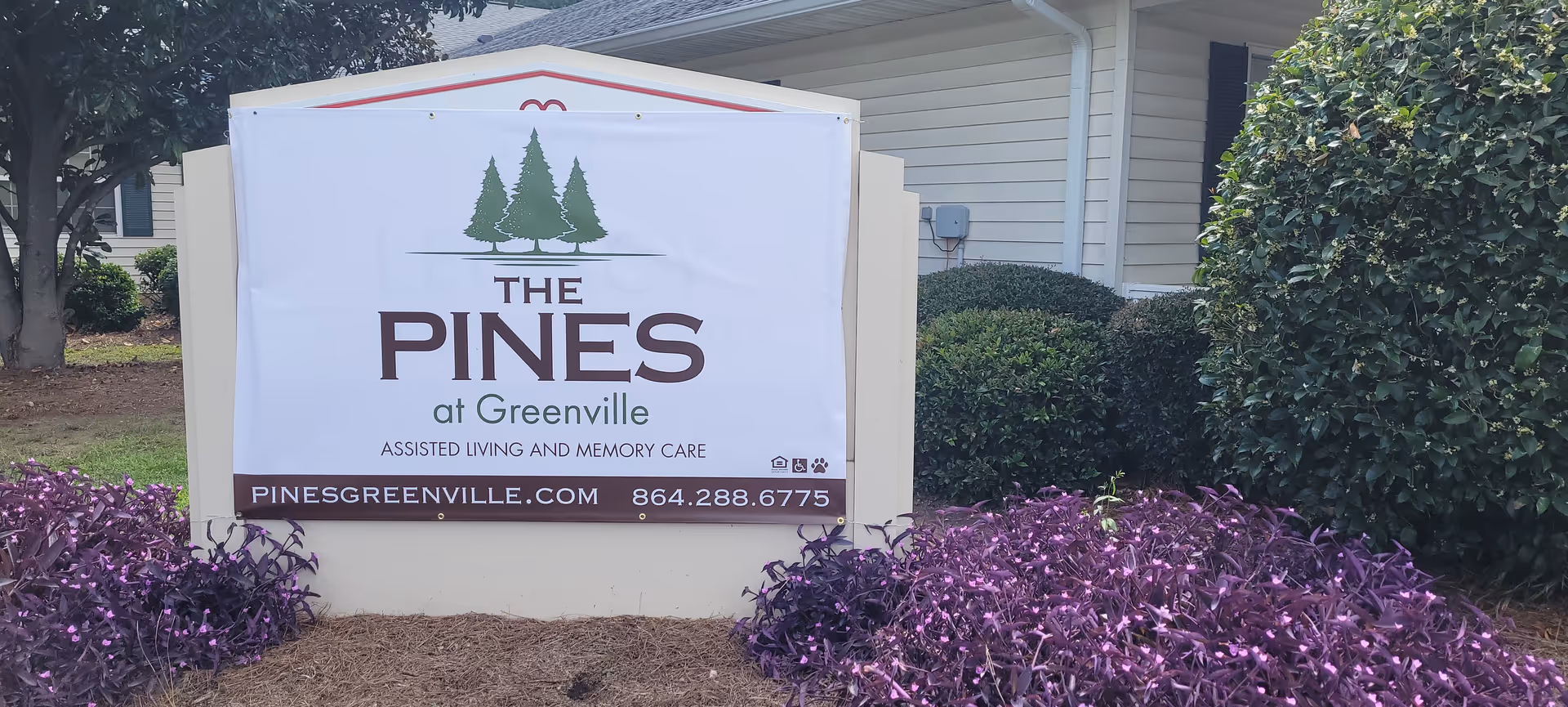 Outdoor sign for The Pines at Greenville Assisted Living and Memory Care with purple groundcover.