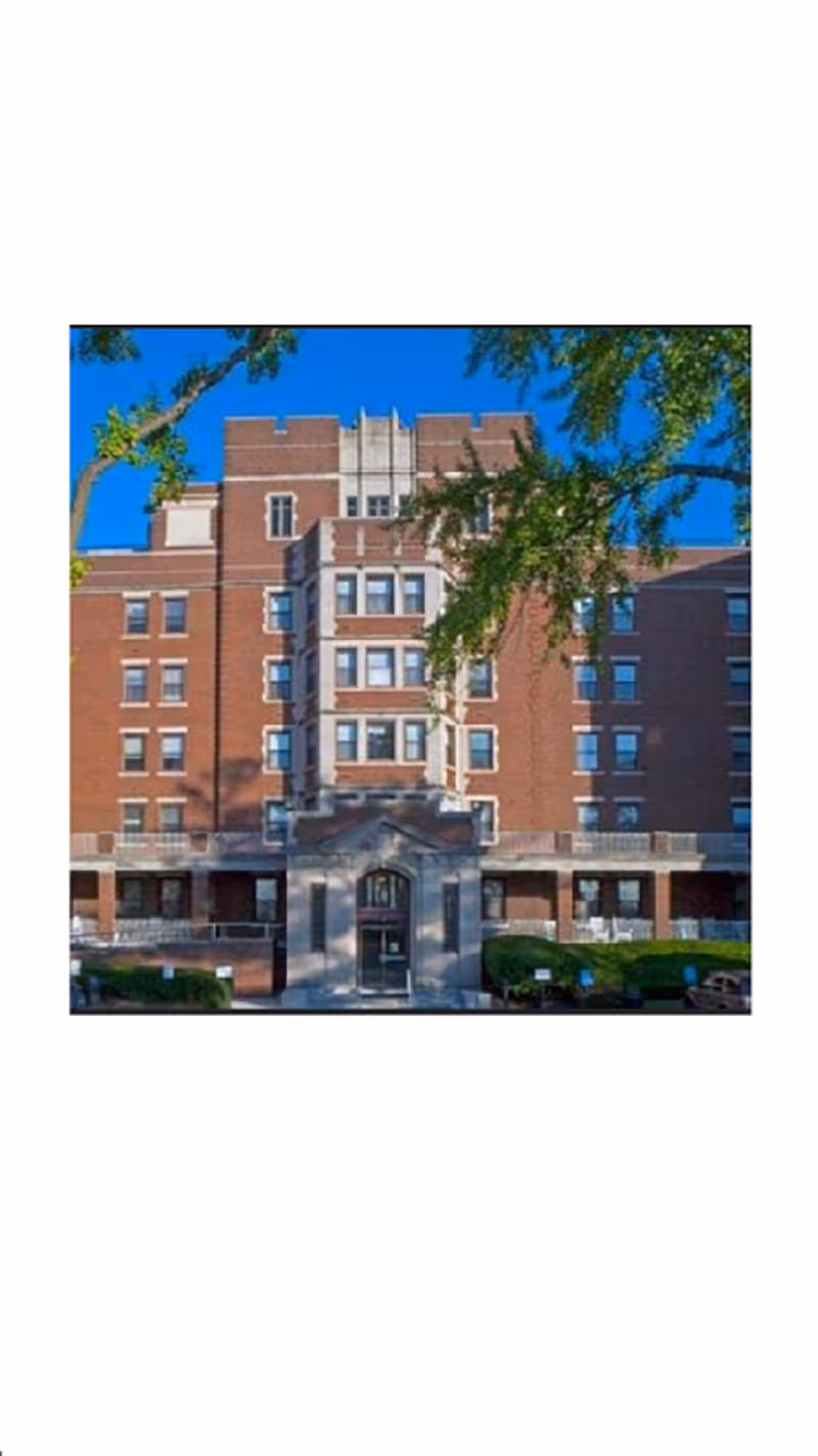 Exterior view of Deer Meadows Retirement Community building with central entrance, brick facade, and surrounding trees.