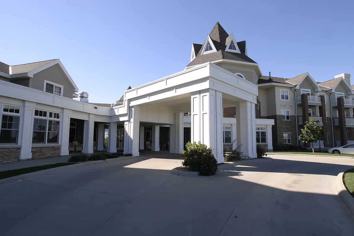 Covered entrance and driveway leading to the multi-story front of a senior living facility with a turret and balconies.