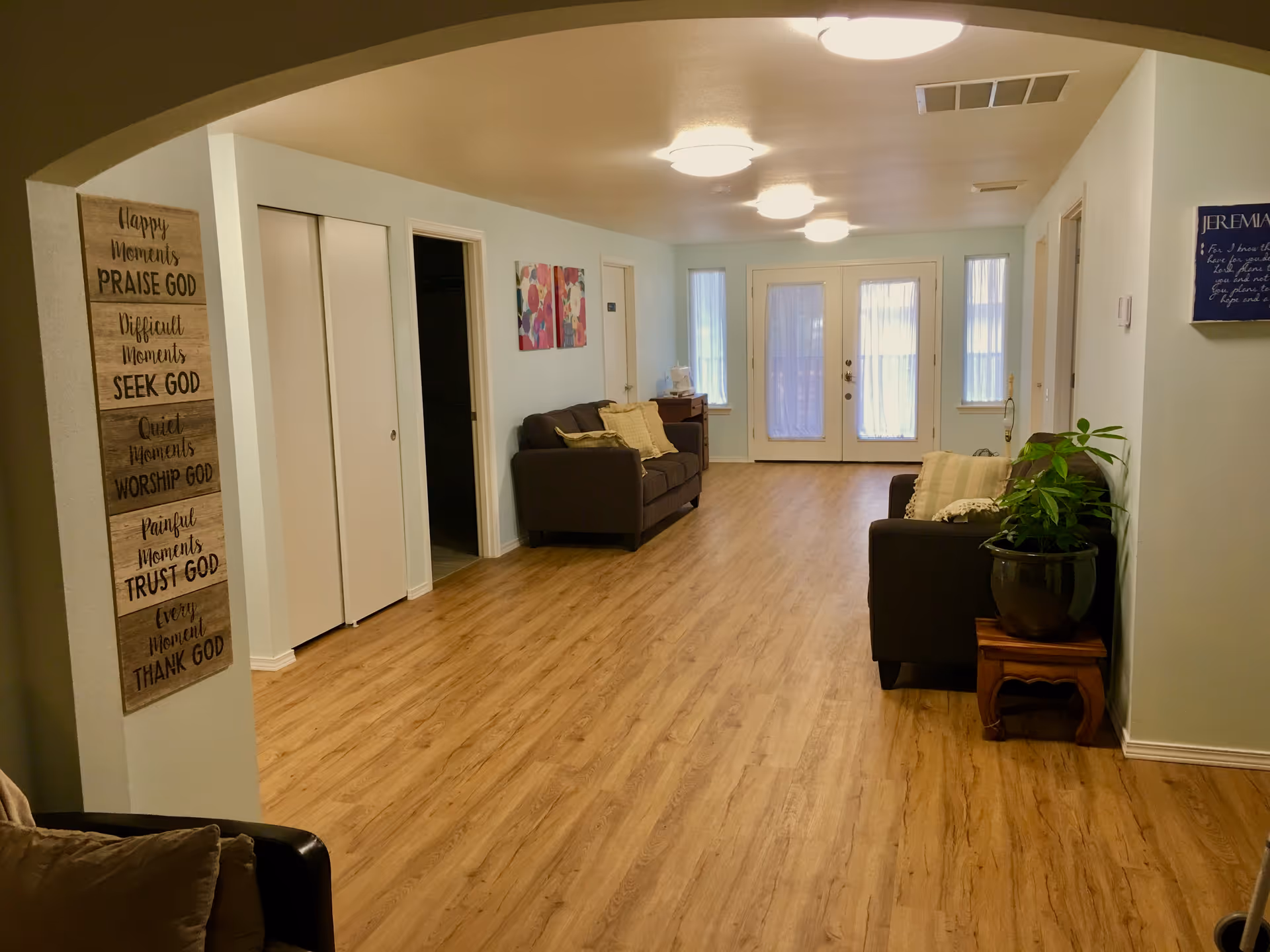 Bright communal living room with couches, plants, wall art, and glass doors at the end.