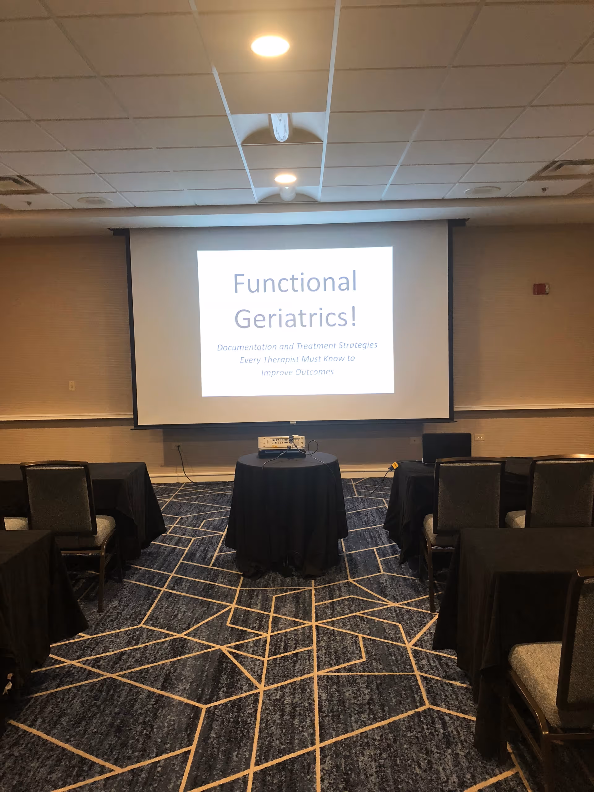Conference room setup with projector screen showing 'Functional Geriatrics!' and tables