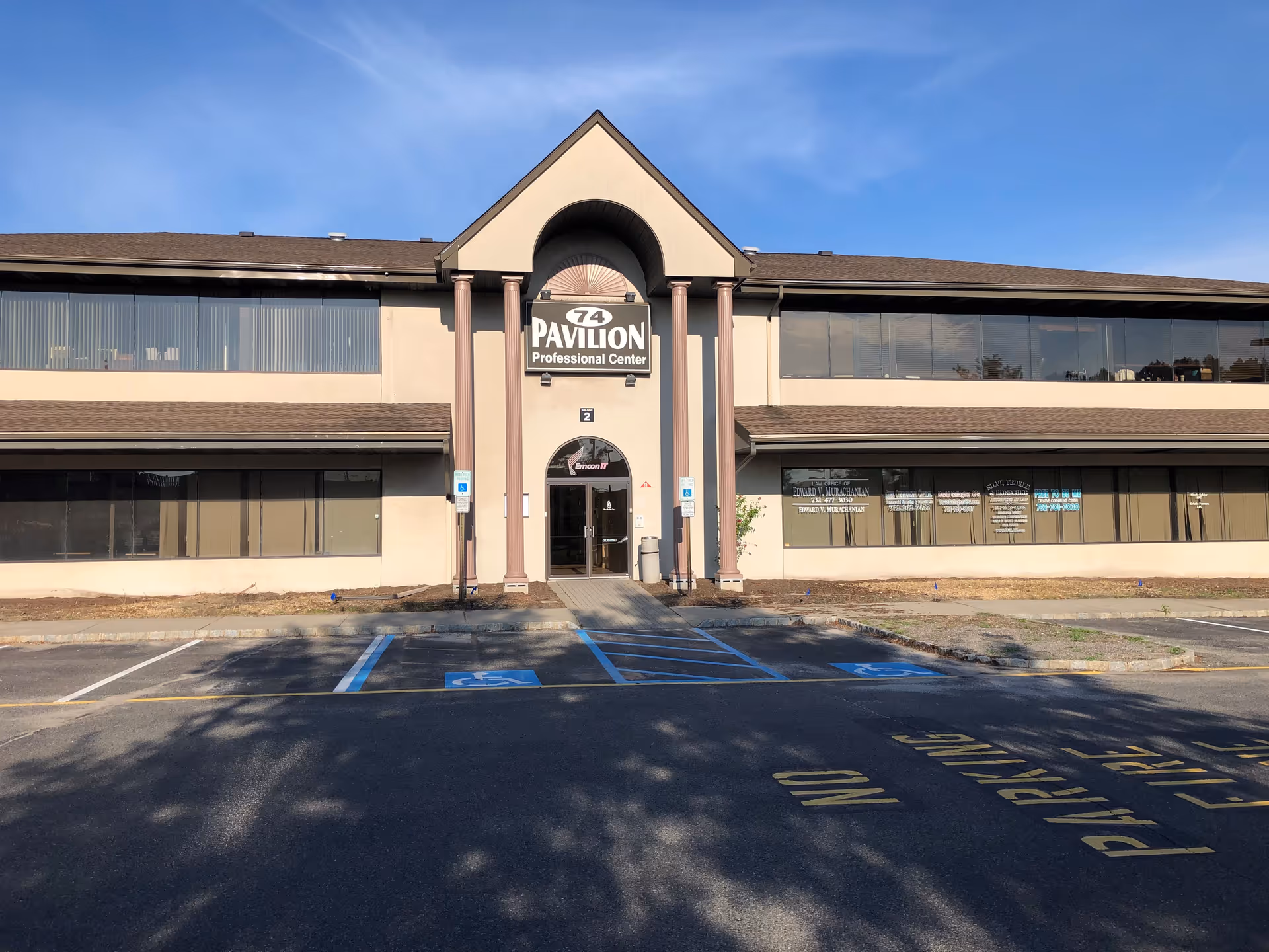 Two-story commercial building with central arched entrance and front parking lot.