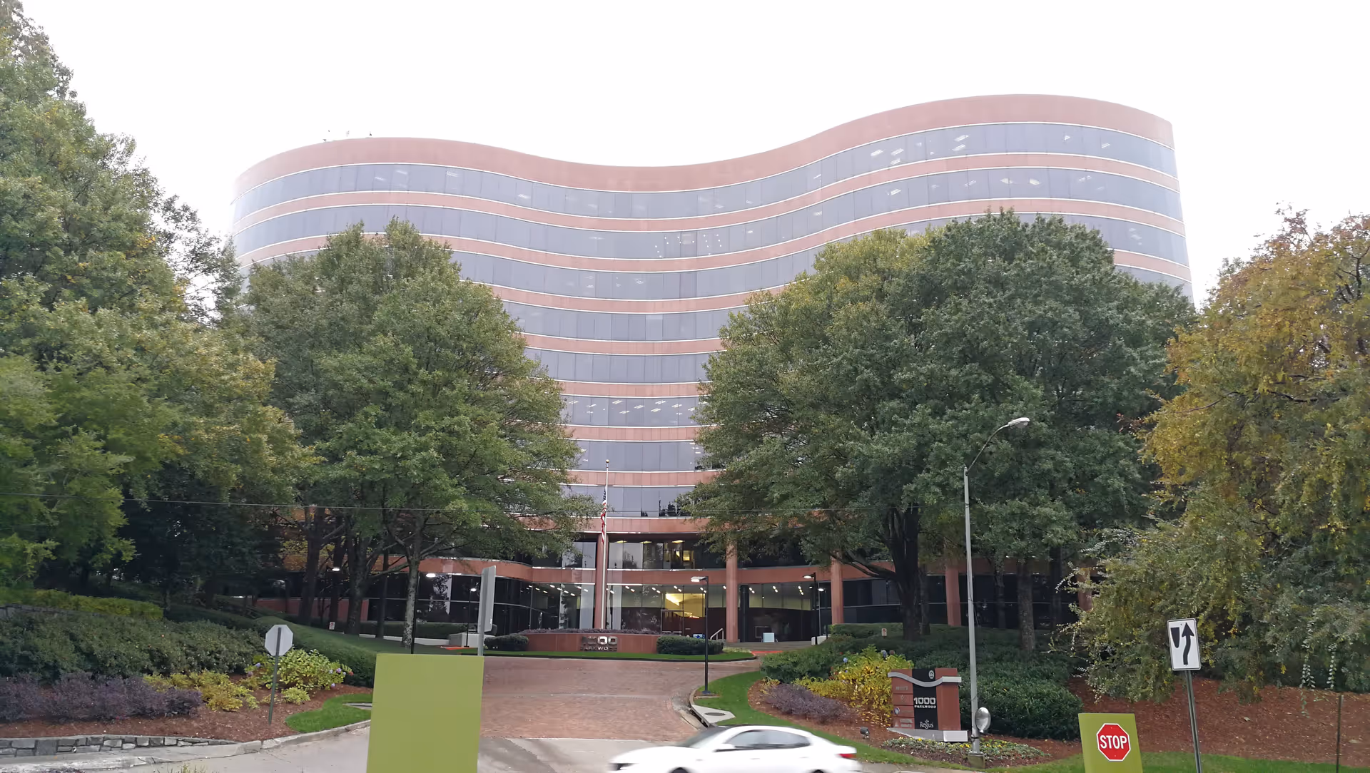 Curved glass facade of Avant Care exterior framed by trees and a driveway.