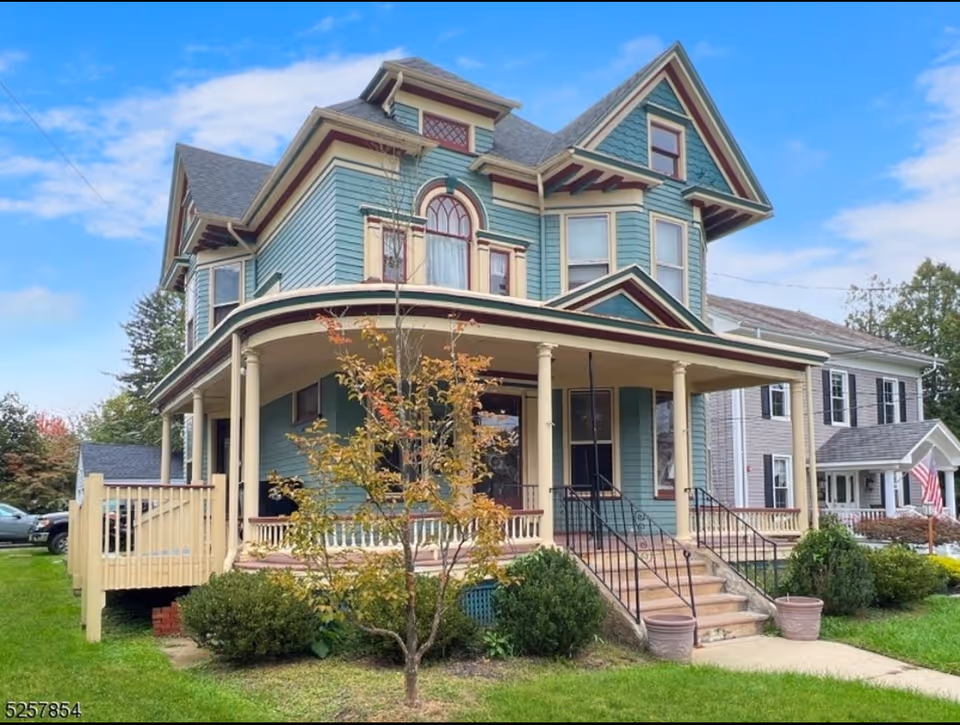 A large teal Victorian-style house with a wraparound porch and front steps.