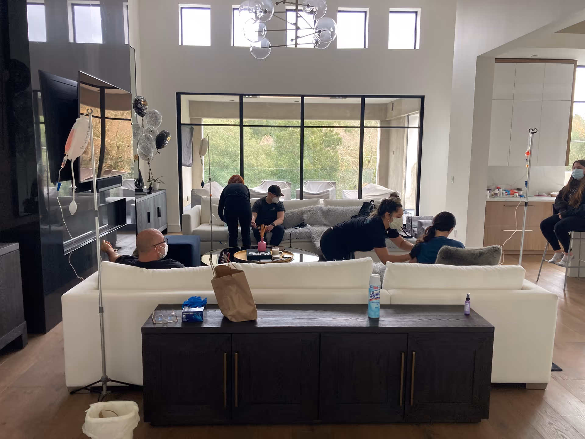 Residents and staff gather in a bright living room, with equipment nearby for assistance.