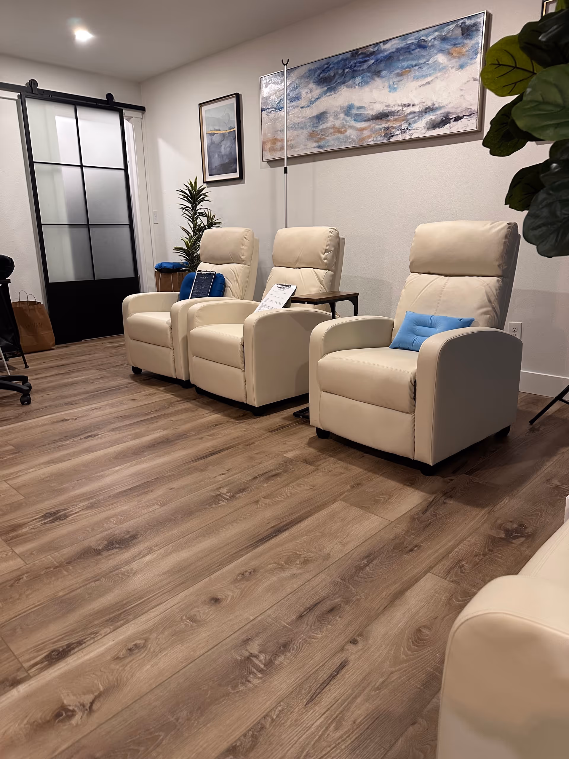 Three beige recliner chairs are arranged in a waiting lounge with art on the walls.